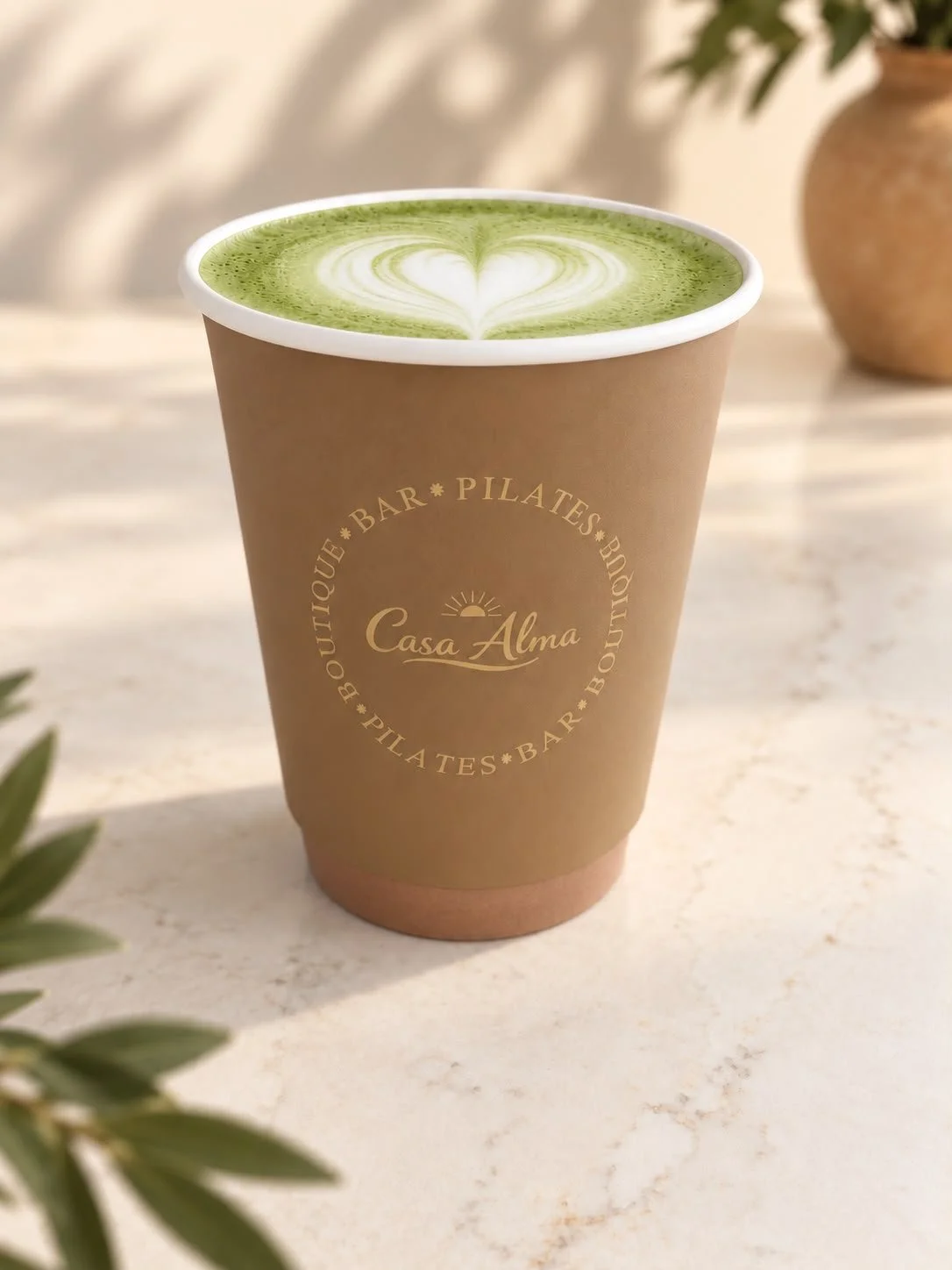 Een papieren Casa Alma bekertje met een matcha latte met hartvormige schuimkunst.