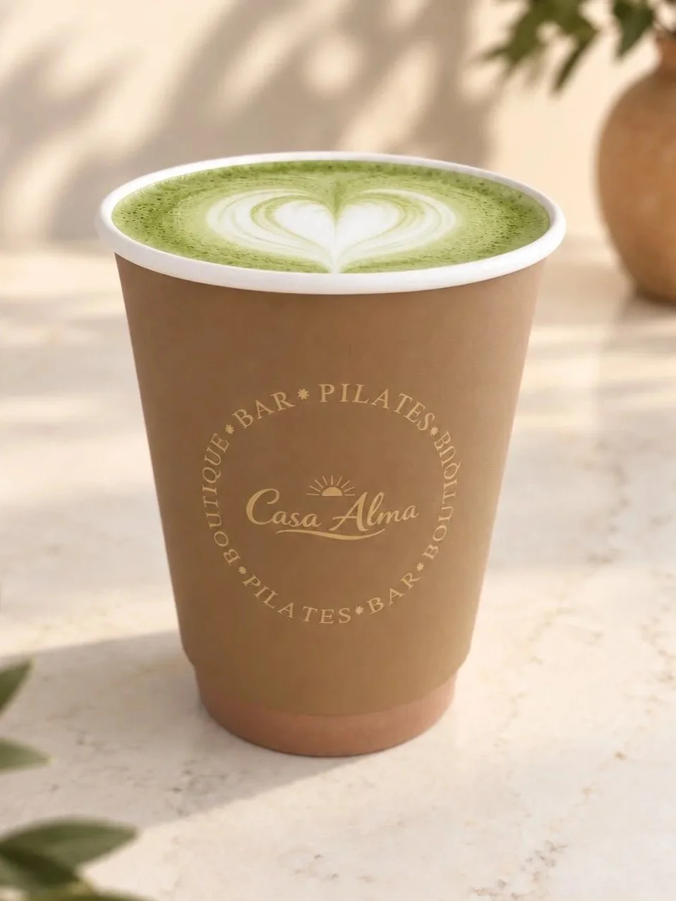 Een papieren Casa Alma bekertje met een matcha latte met hartvormige schuimkunst.