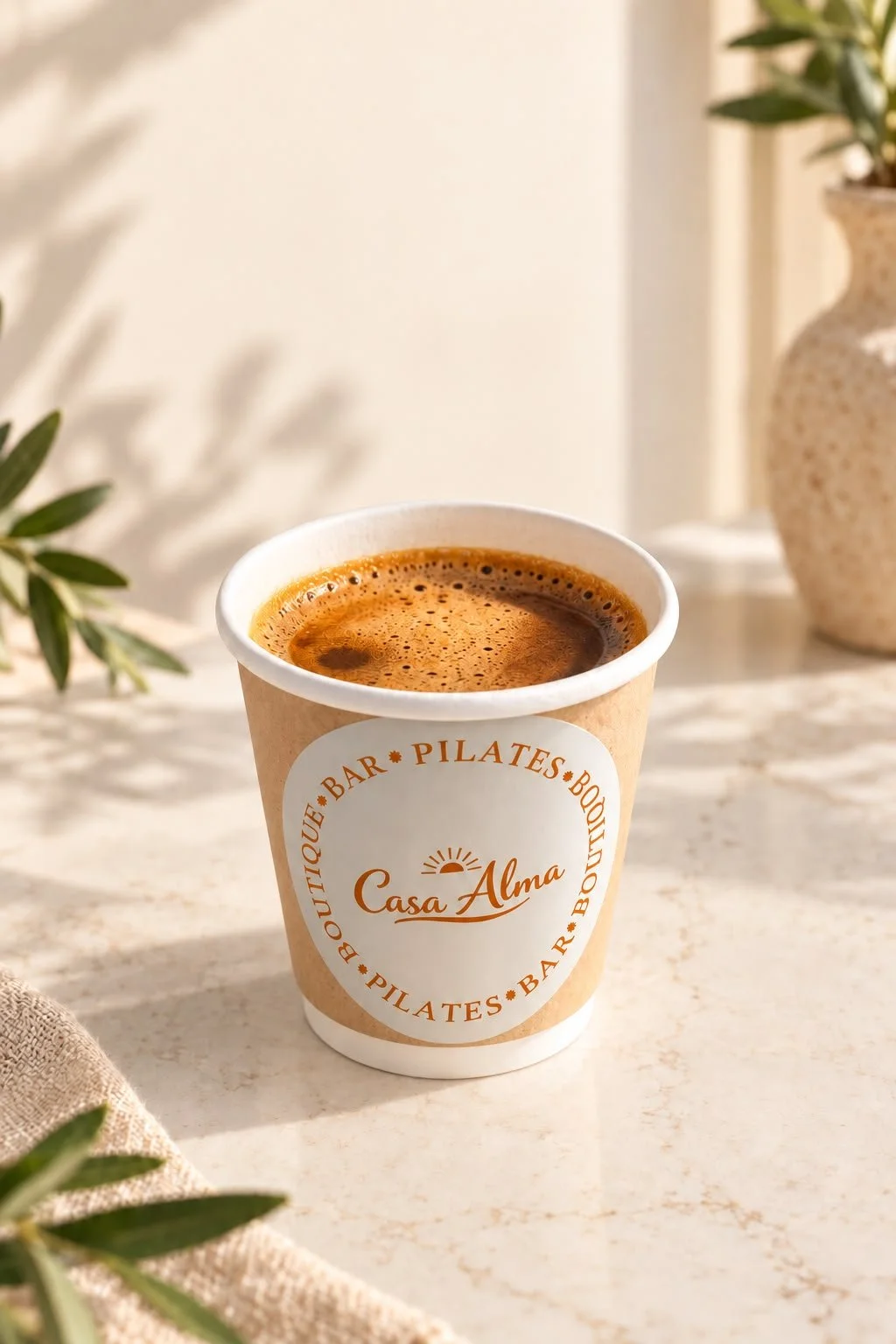 Een kopje specialty koffie (espresso) op een tafel met een label dat 'Casa Alma' zegt, omgeven door planten en decoratieve vazen in een lichte, natuurlijke setting.