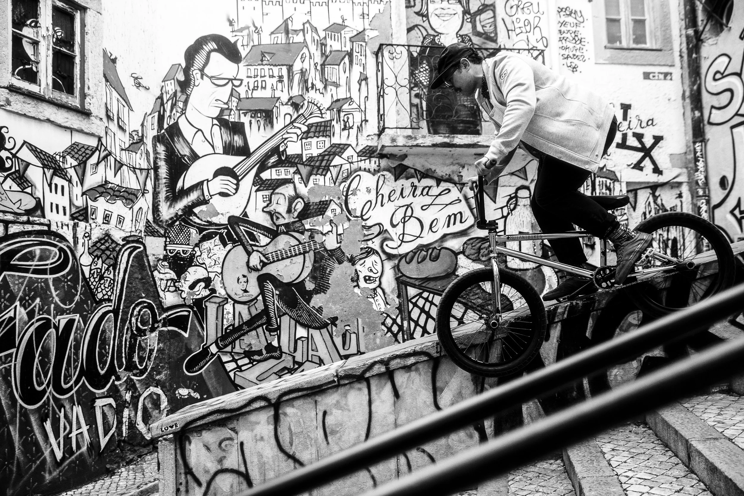 Mensch auf BMX vor einer Wand mit Graffiti. Graffiti zeigt Musiker, Häuser und Schriftzüge.