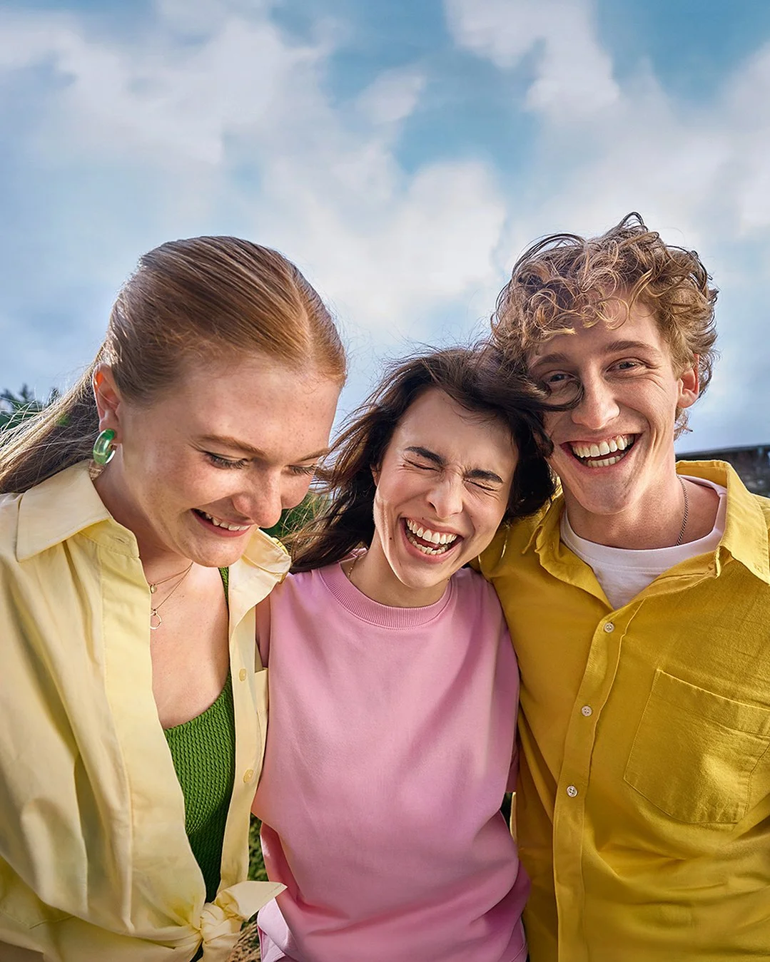 Drei fröhliche junge Menschen lachen zusammen im Freien bei schönem Wetter.