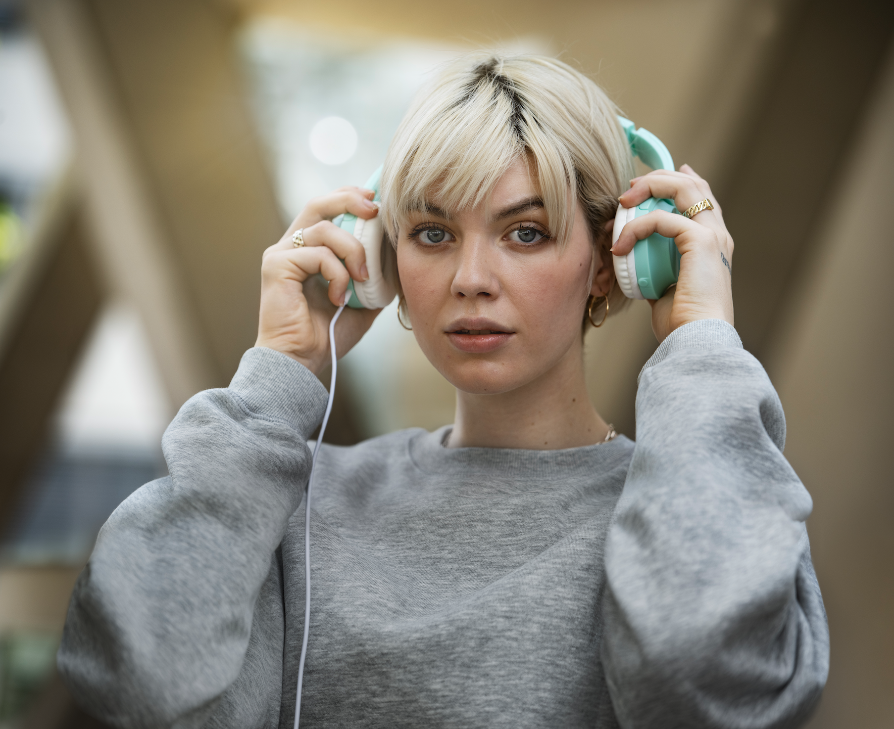 Junge Frau mit Kurzhaarschnitt trägt Kopfhörer und schaut in die Kamera.