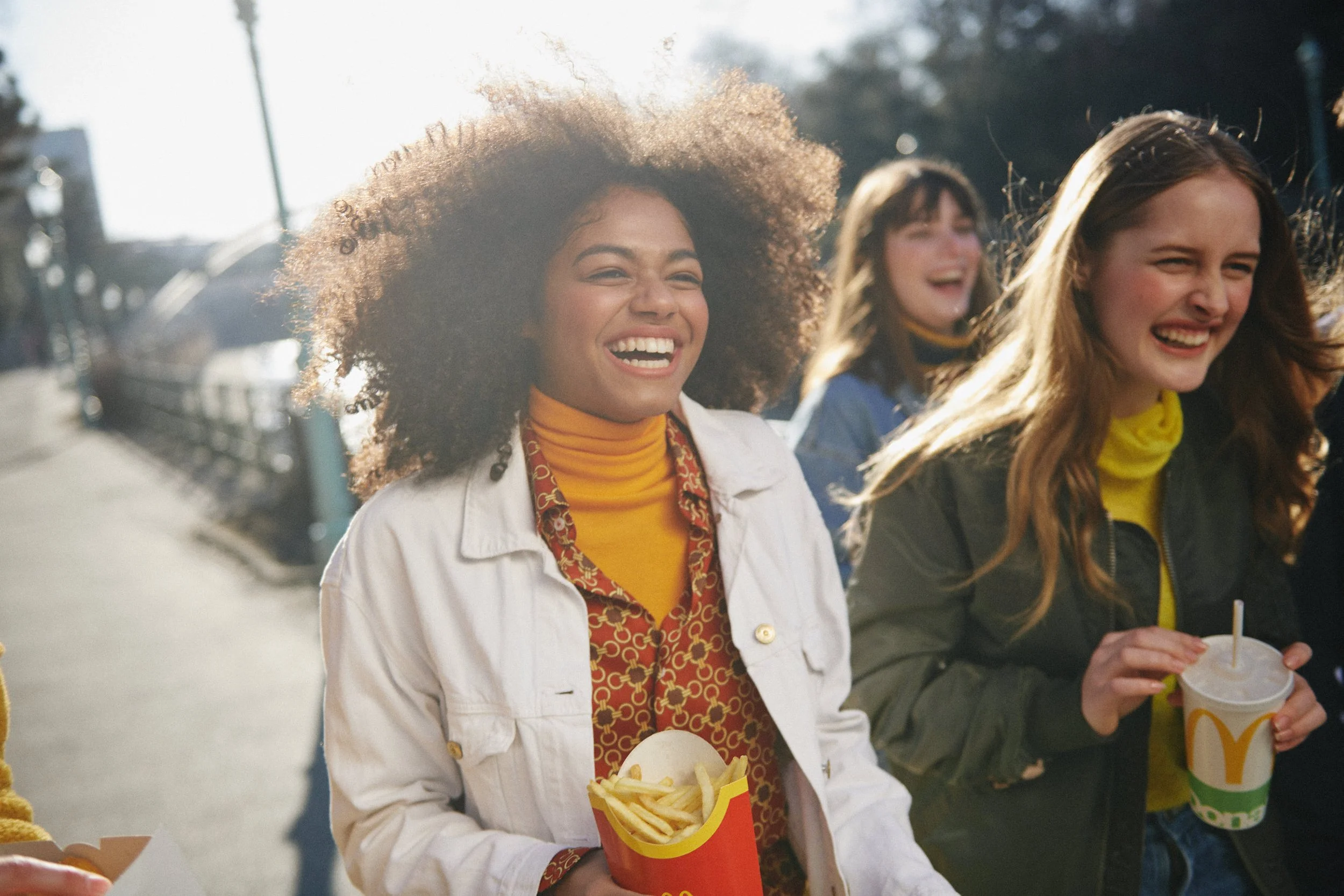 Freudige junge Frauen, die McDonald's Essen wie Pommes und Getränke genießen, draußen an einem sonnigen Tag.