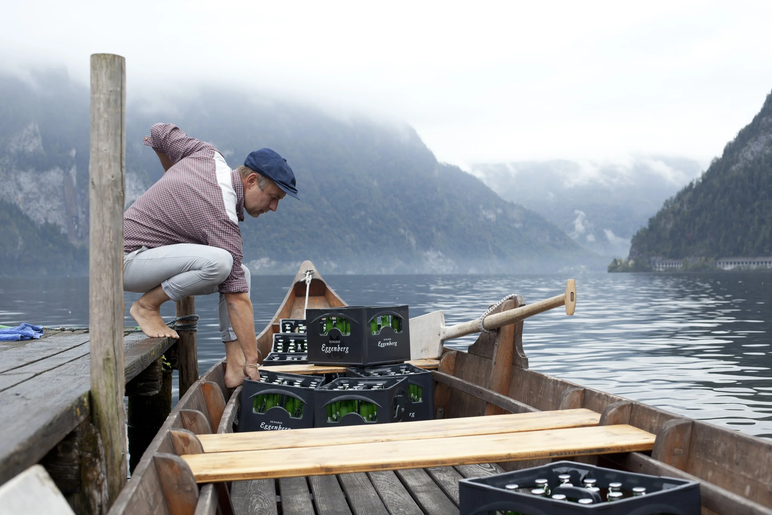 Mann macht Bierbereitstellung auf einem Boot an einem ruhigen See mit Bergen im Hintergrund.