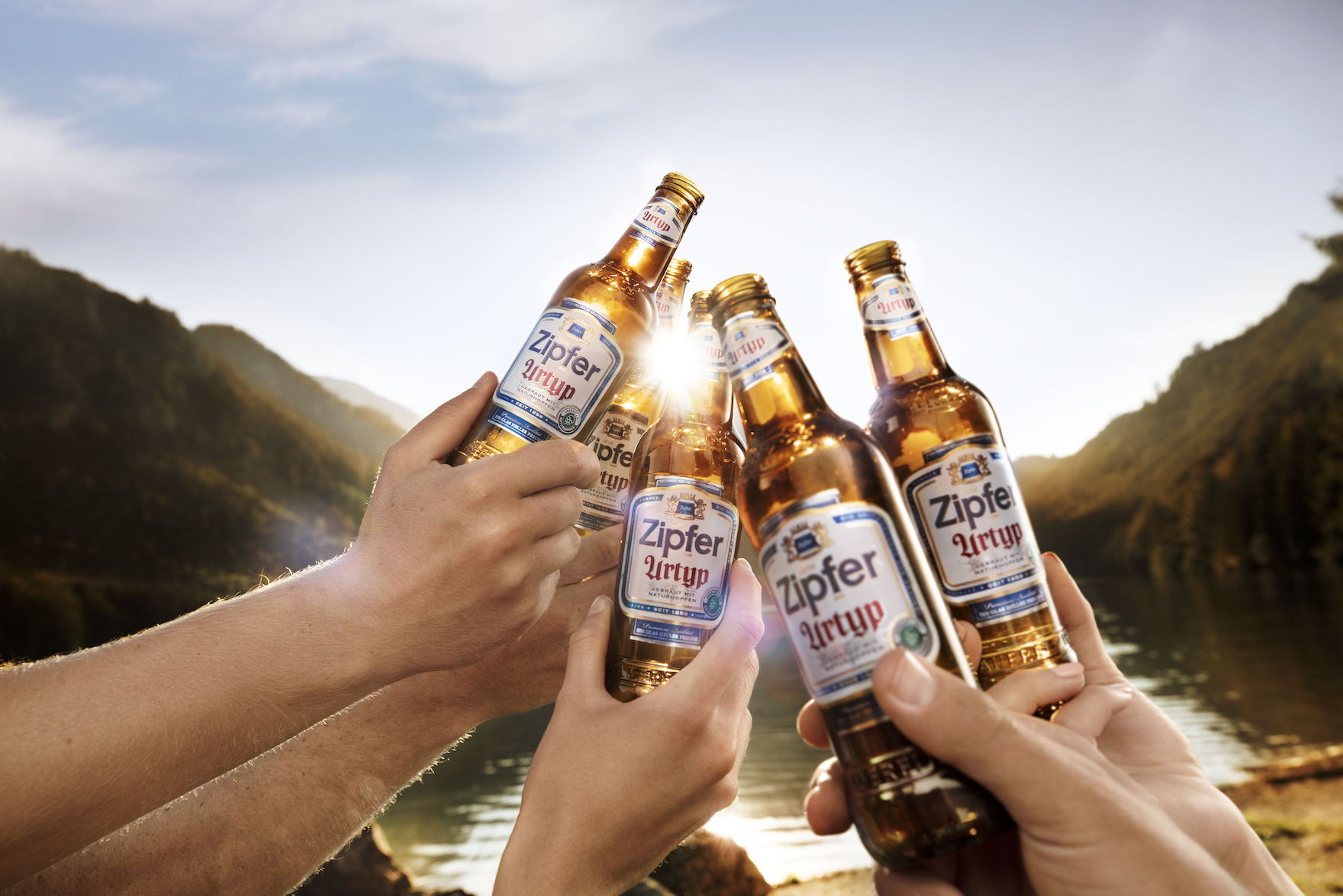 Mehrere Menschen stoßen mit Flaschen Zipfer Urtyp Bier in einer Naturkulisse an.