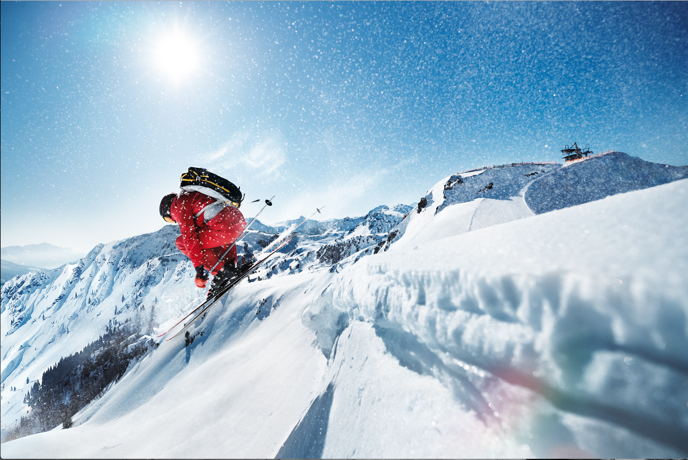 Skifahrer in roter Jacke bergab auf verschneiter Piste bei strahlendem Sonnenschein in den Bergen.