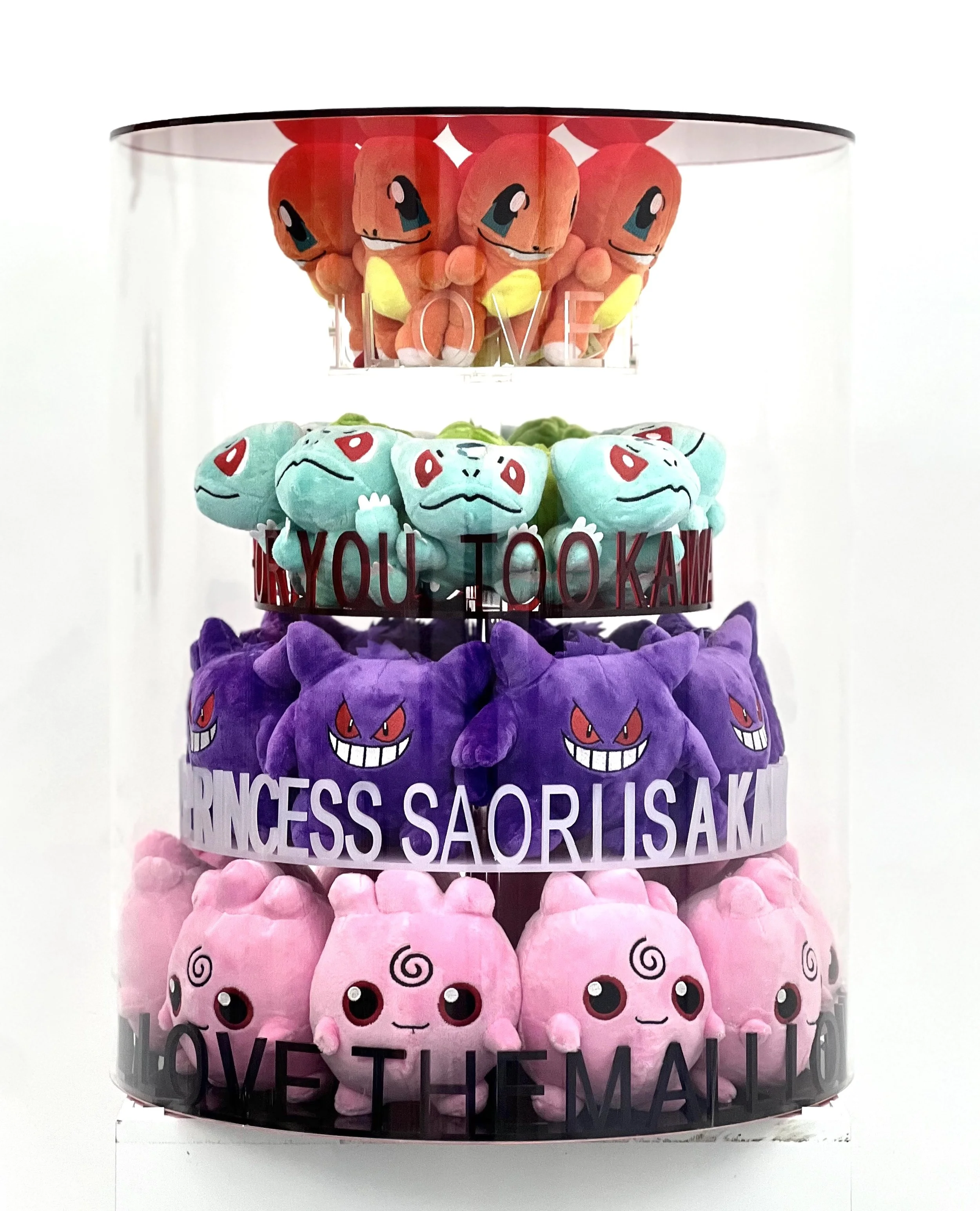 Four tiers of colorful plush toys resembling Pokémon characters, with motivational words on each tier, in a clear acrylic display case.
