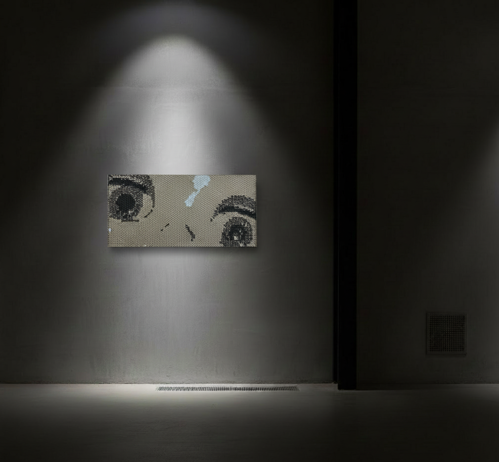 Black and white portrait of a woman's eyes and nose, displayed on a small pixelated canvas on a gray wall, illuminated by a focused light.
