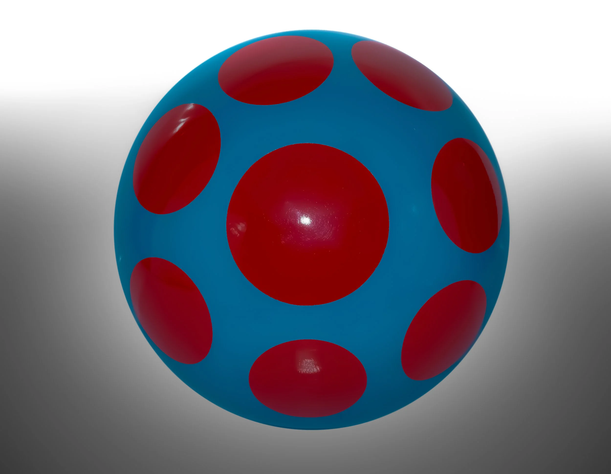 A colorful ball with a blue surface and red polka dots.