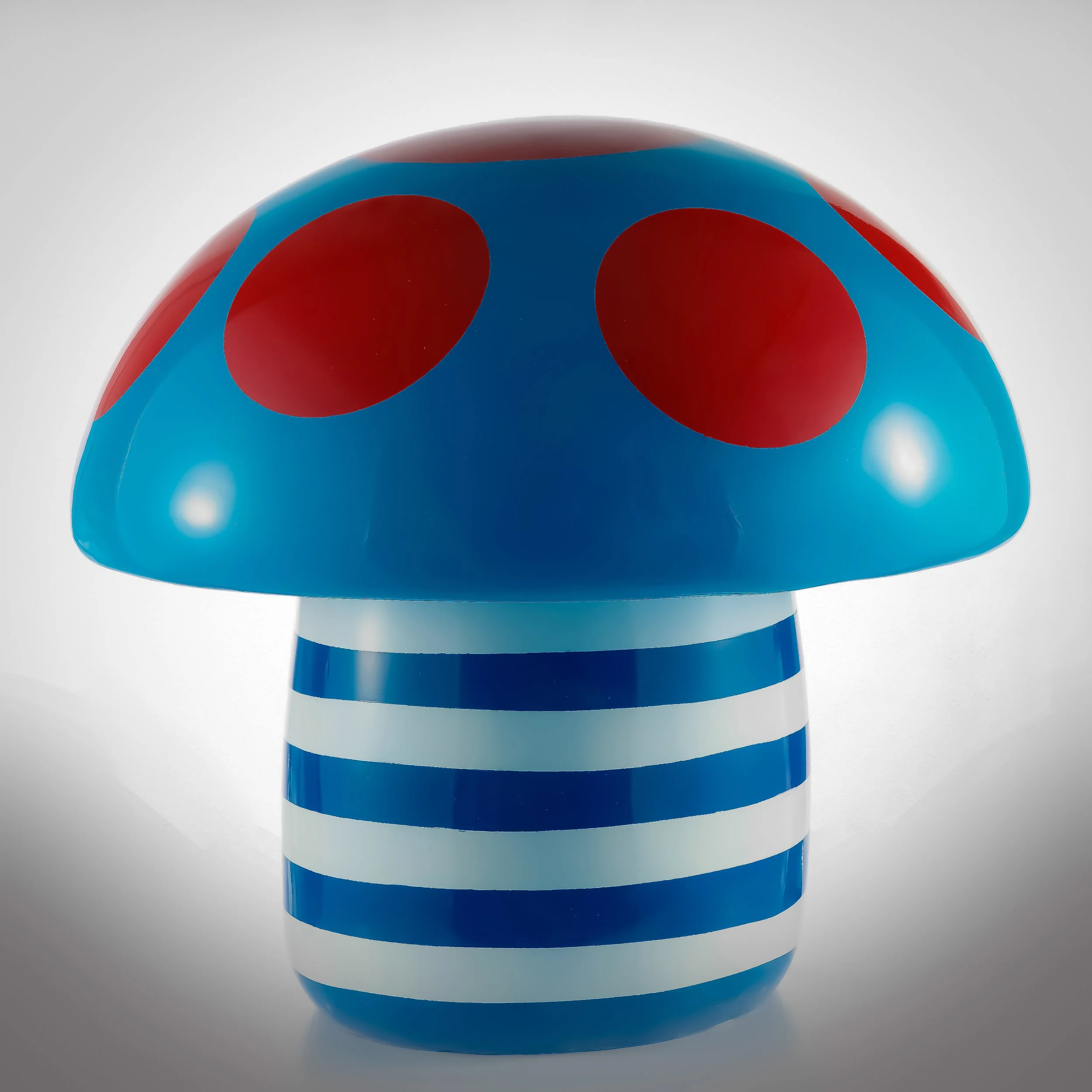 A decorative lamp shaped like a mushroom with a blue cap with red spots and a striped blue and white stem.