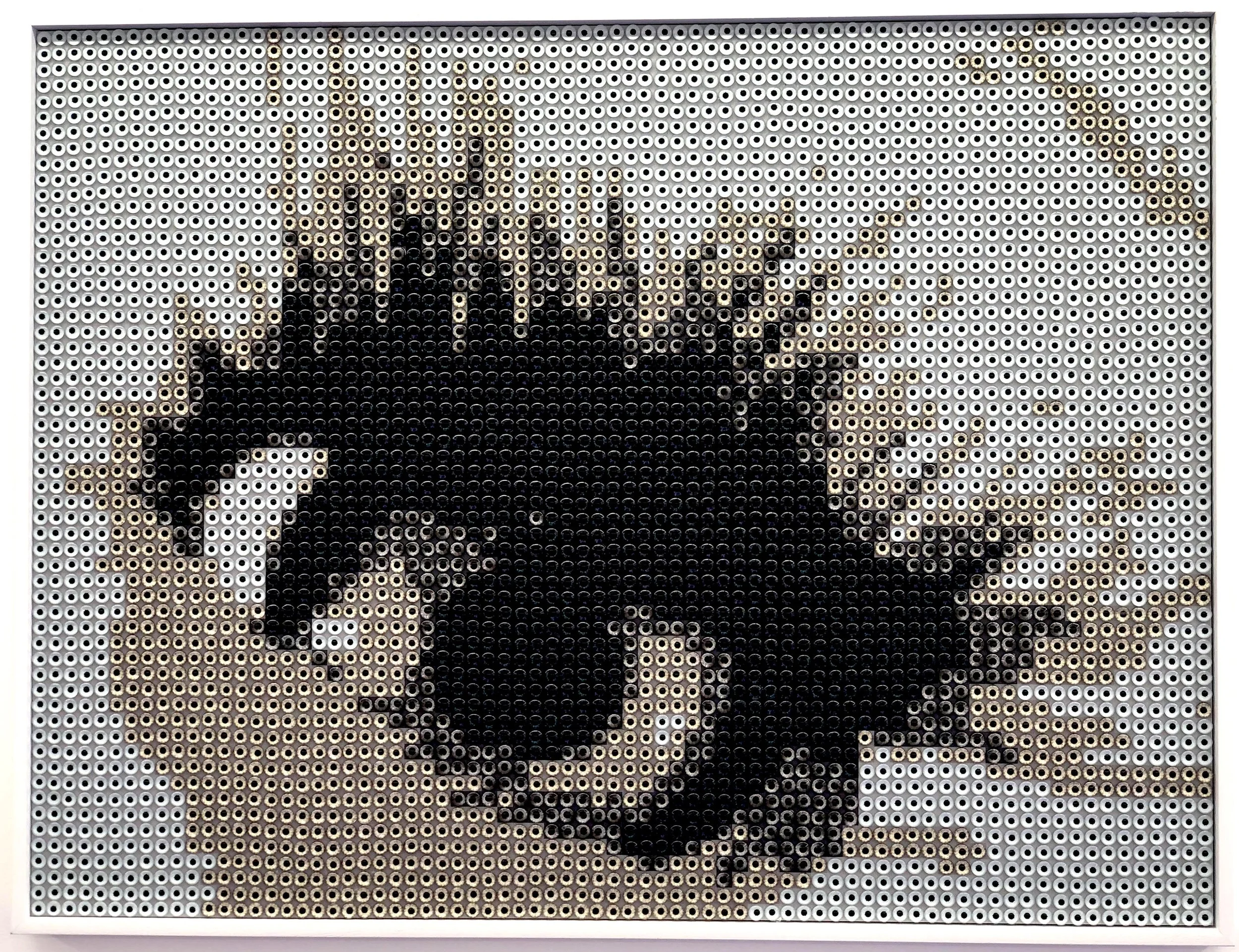 A mosaic of a skull with black, beige, and gray beads. The skull features dark eye sockets and a prominent jaw, with a background of scattered beige beads.