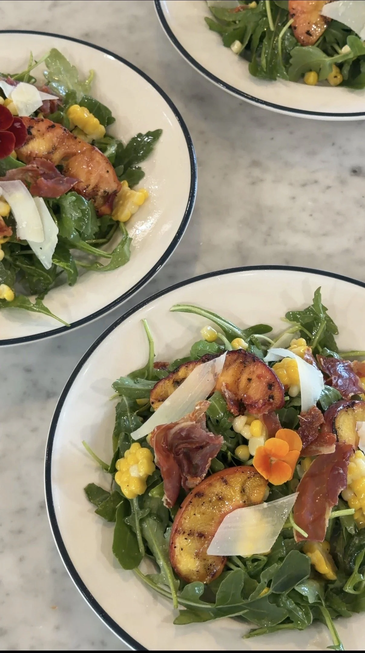 Arugula salad with grilled peaches, sweet corn, crispy prosciutto, shaved Parmesan, and an edible flower, served at a private chef dinner in Westport, Massachusetts