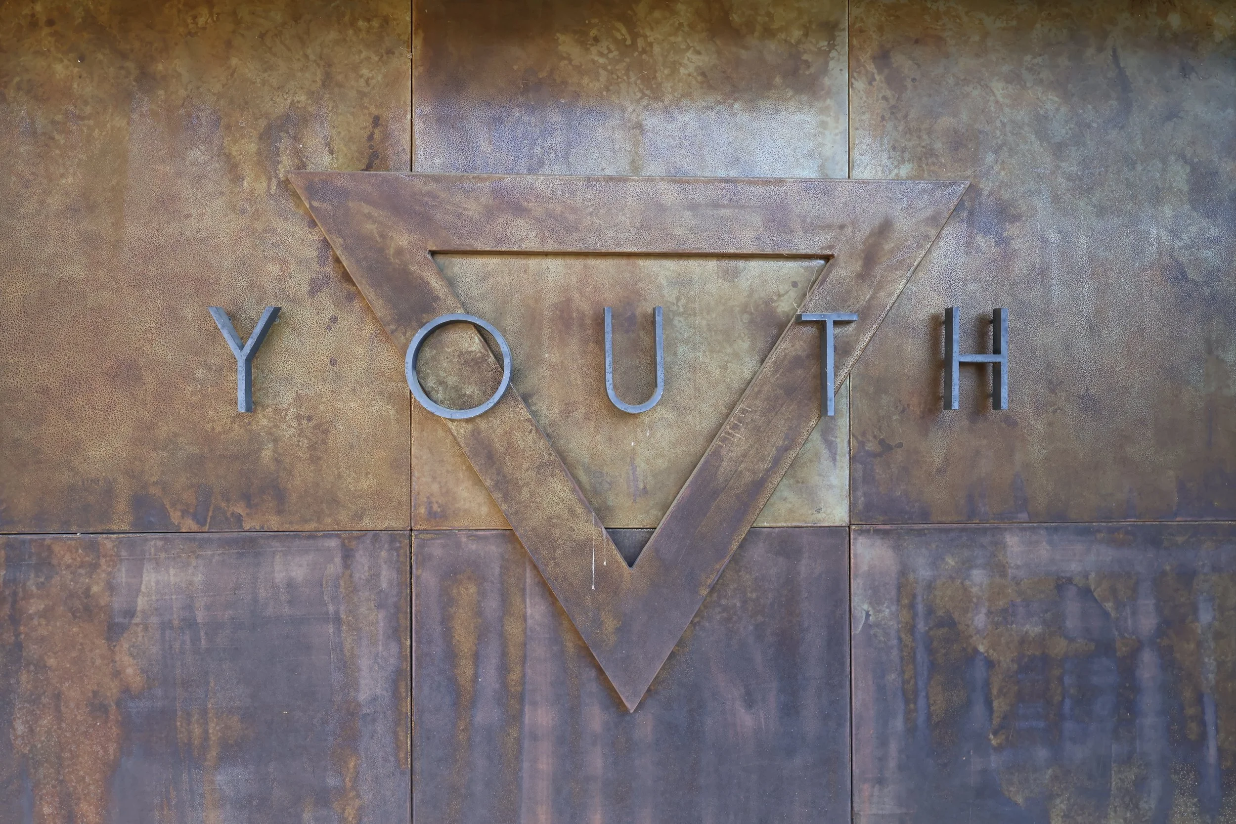 Metal wall decoration with a downward-pointing triangle and the word 'YOUTH' spelled out in individual metal letters.