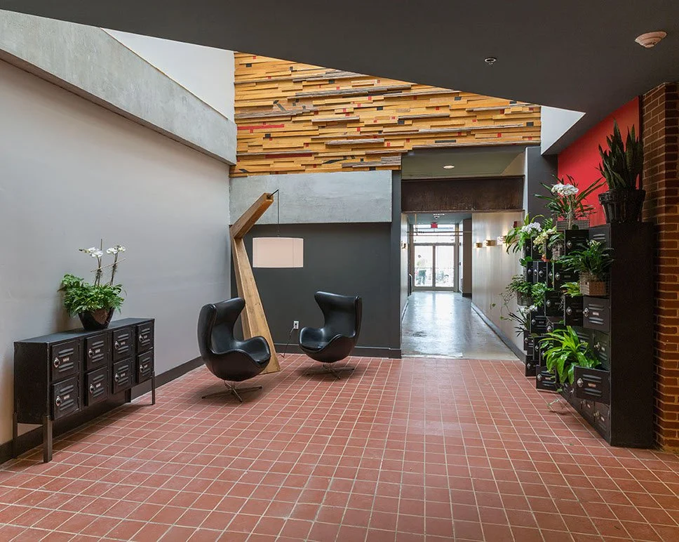 Modern lobby with black chairs, plant-filled shelves, and a wooden accent wall.