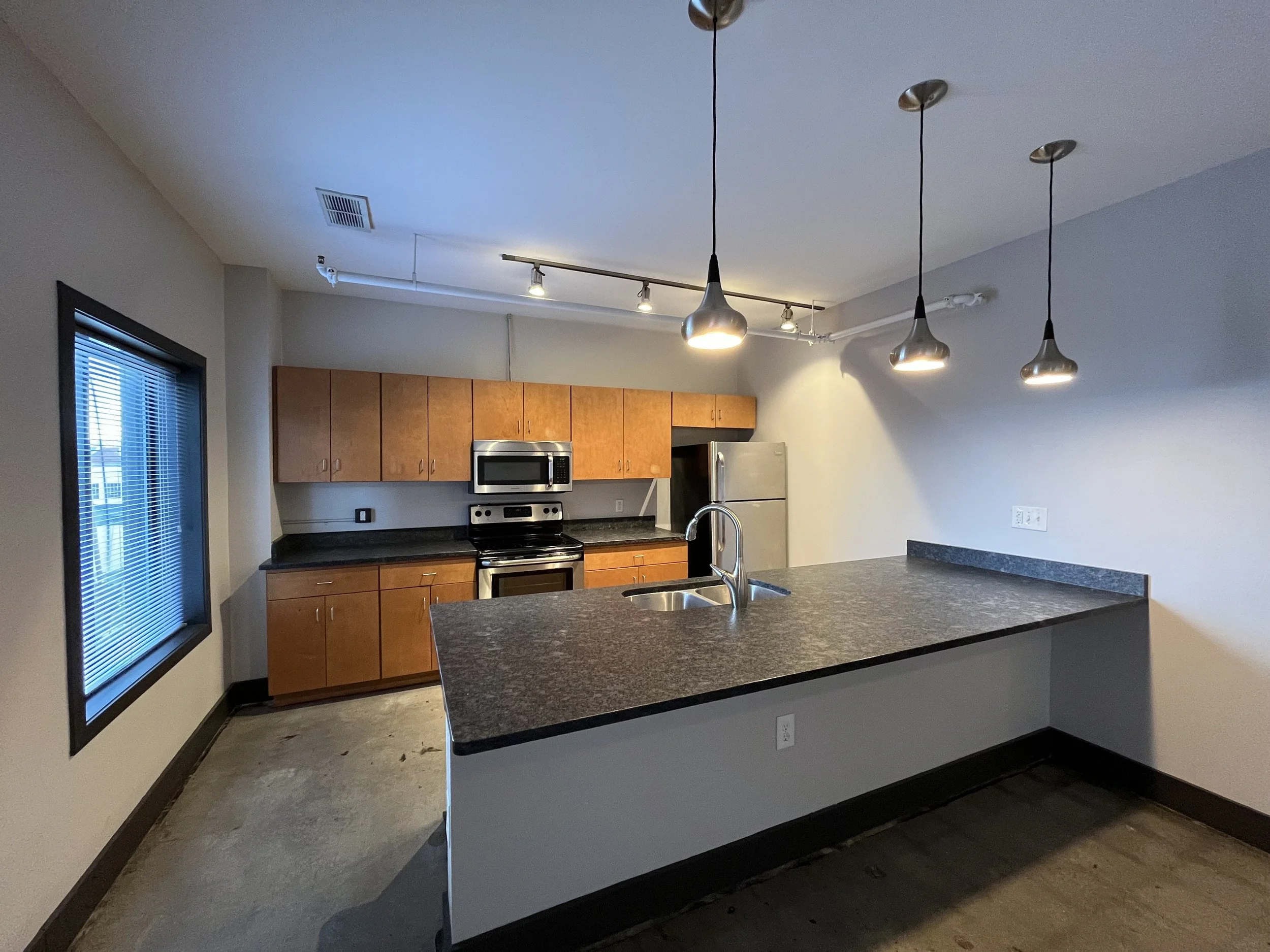 Modern kitchen with pendant lights, wooden cabinets, stainless steel appliances, and a granite countertop.