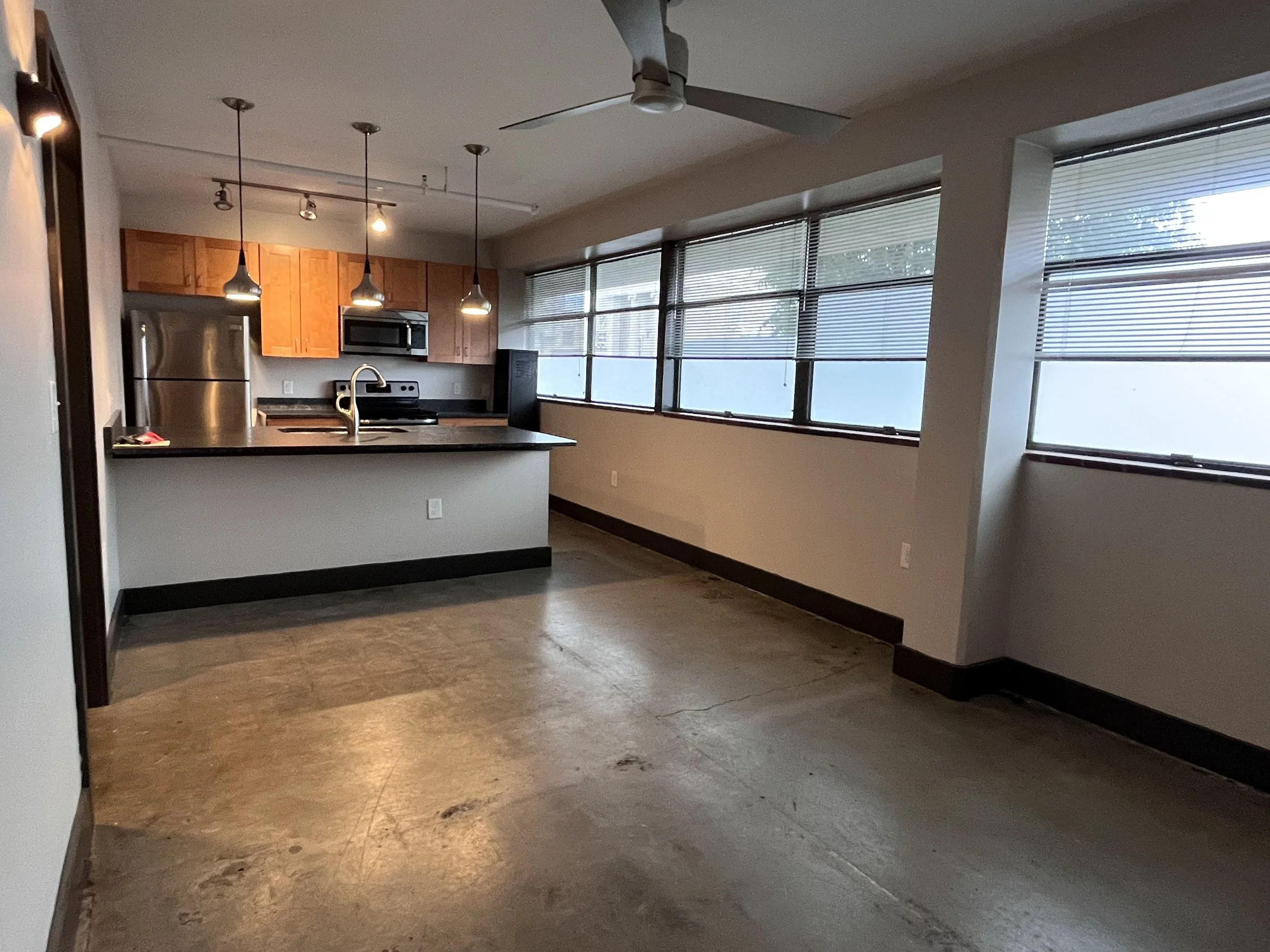 Empty apartment with large windows, wooden kitchen cabinets, and a gray countertop.