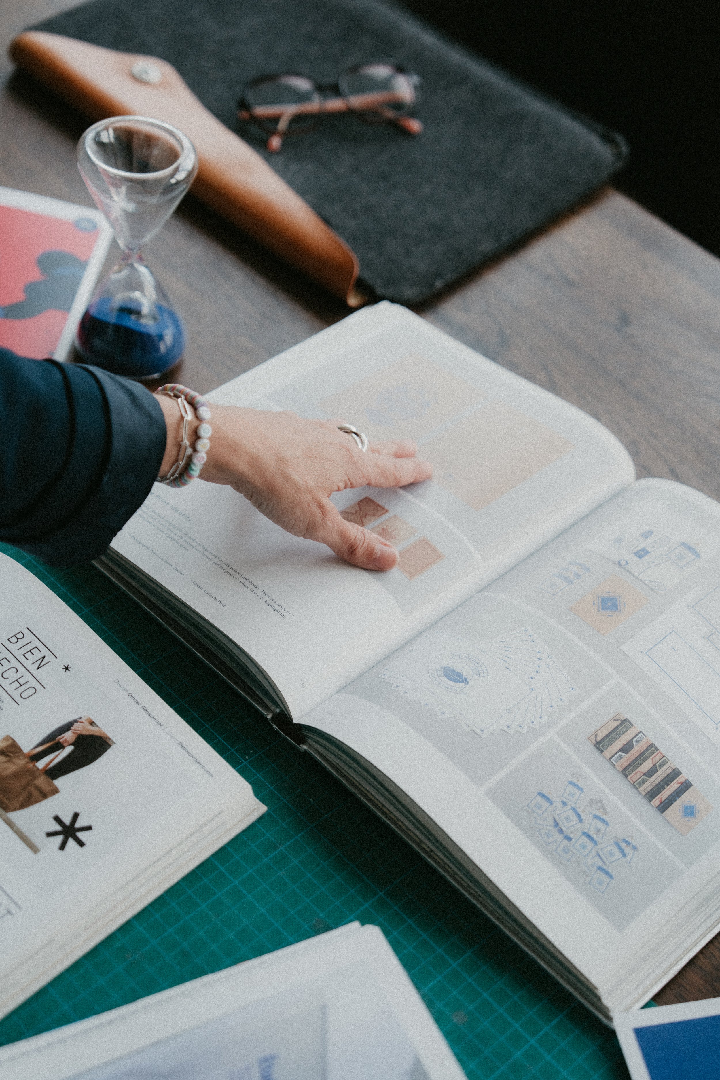 Un bureau avec un cahier ouvert montrant des schémas et des illustrations, un verre d'heureux, des lunettes, une tablette, et des brochures.