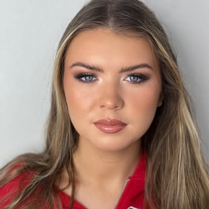A woman with long blonde hair wearing a red top, looking directly at the camera.