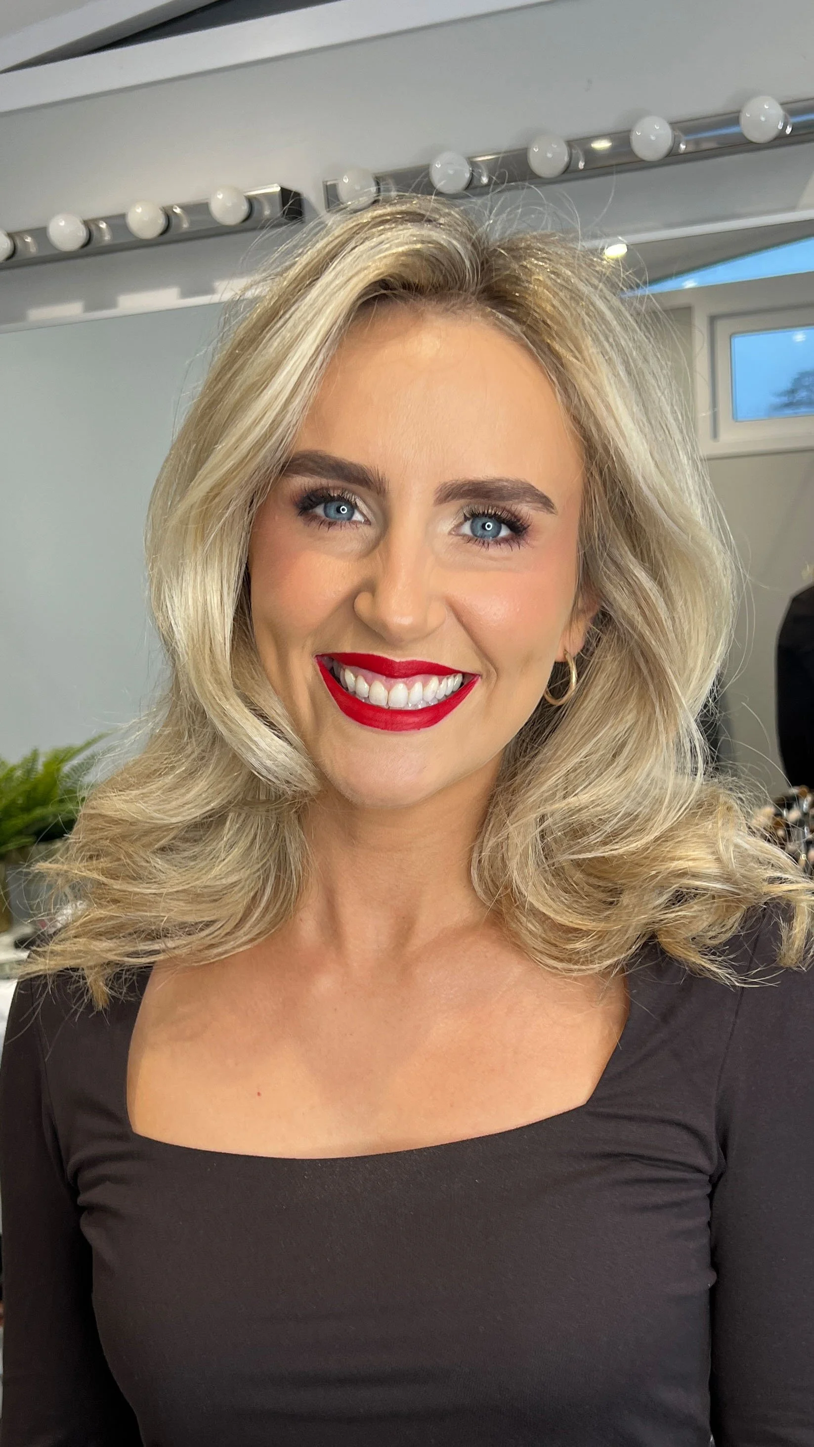 A woman with blonde hair styled in an elegant updo, wearing a navy blue sweater, smiling softly in a bright, modern home kitchen.
