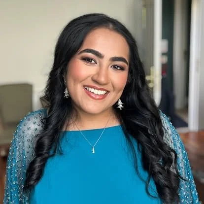 A young woman smiling with long dark hair, wearing a blue dress with sparkly off-shoulder sleeves and star-shaped earrings.