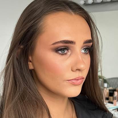 Close-up of a young woman with long brown hair and makeup, looking to the side.