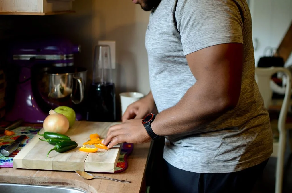A person chopping yellow and orange bell peppers on a wooden cutting board in a kitchen.
