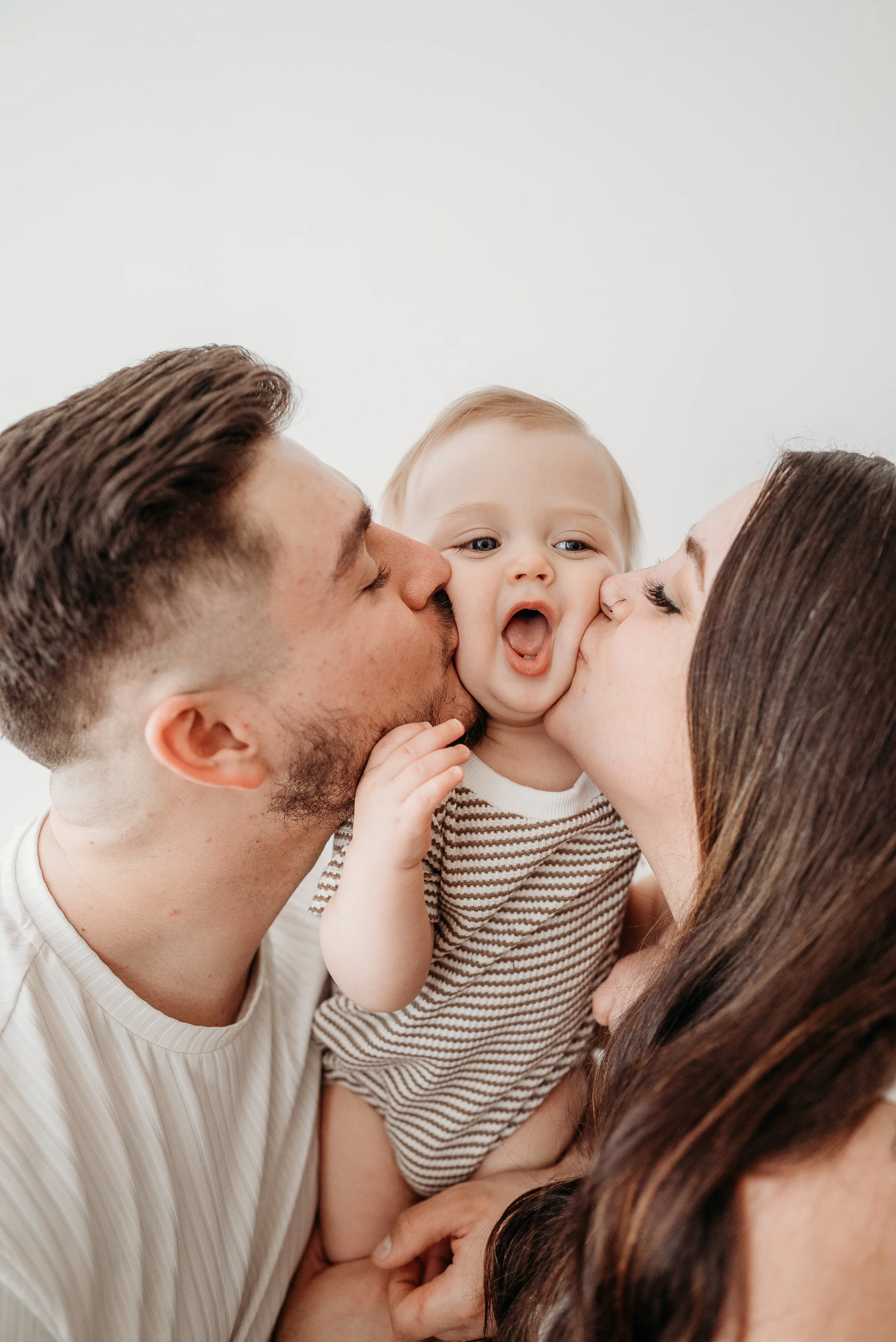 Young family group of two adults and one child sharing kisses.