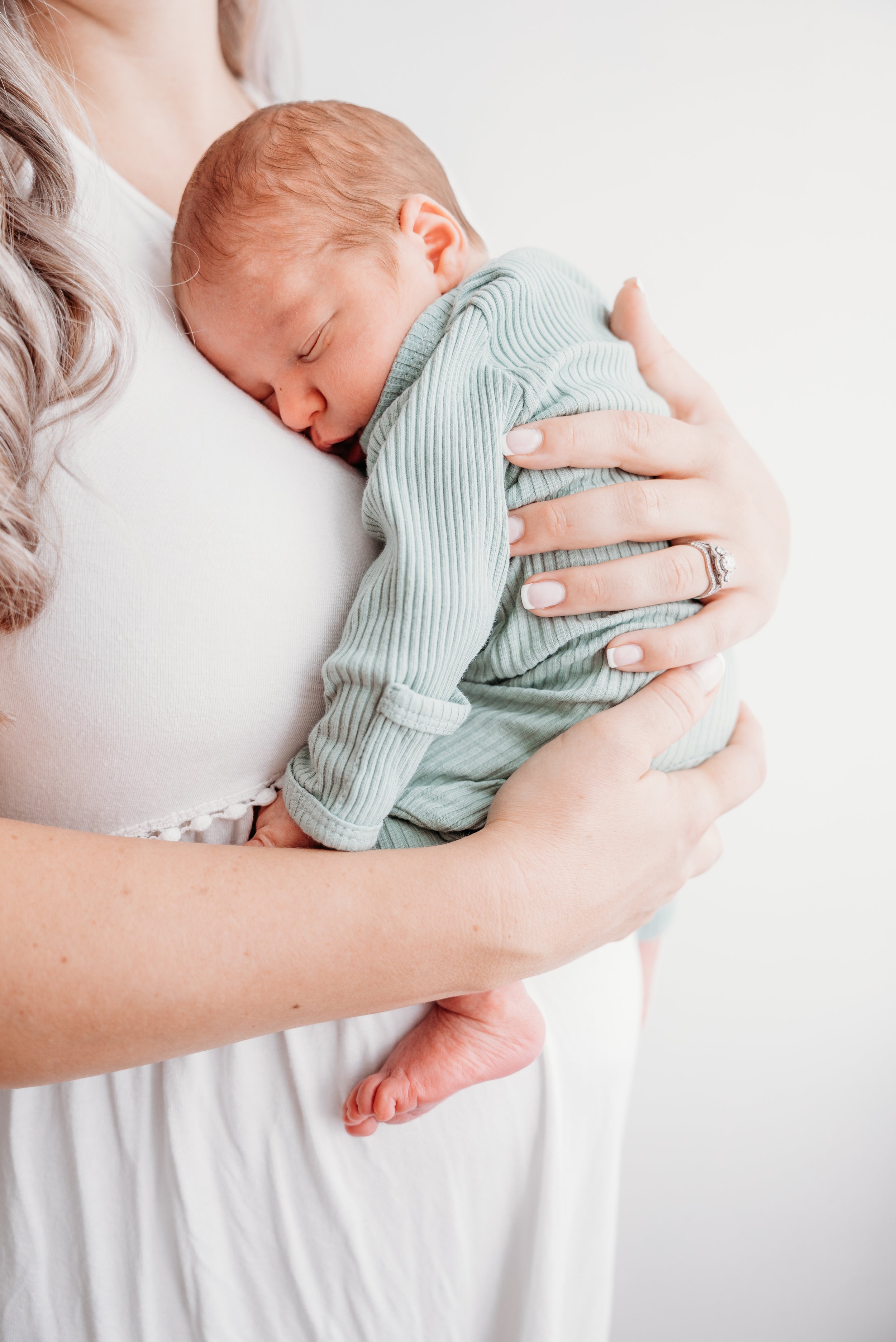 A newborn baby sleeping peacefully on a woman's chest, being held gently with one hand supporting the baby's back and the other hand cradling the baby's bottom.