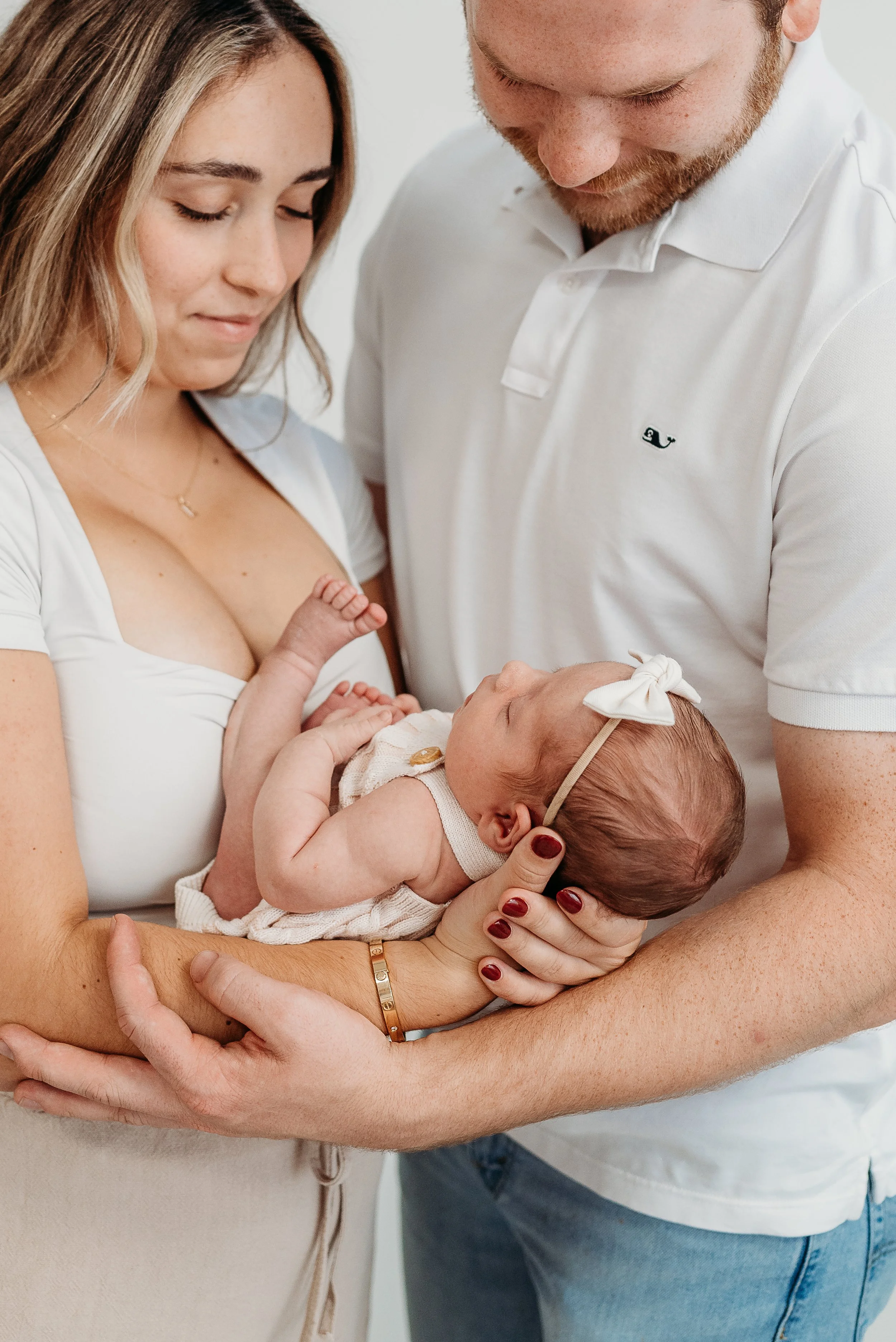 A newborn baby girl being held by her mother, with her father supporting her, in a close-up family portrait.