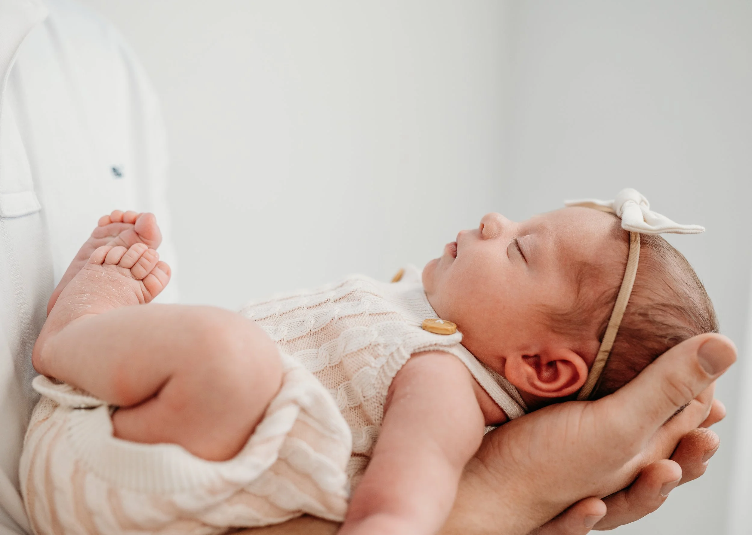 A baby with a headband peacefully sleeping in an adult's hand.