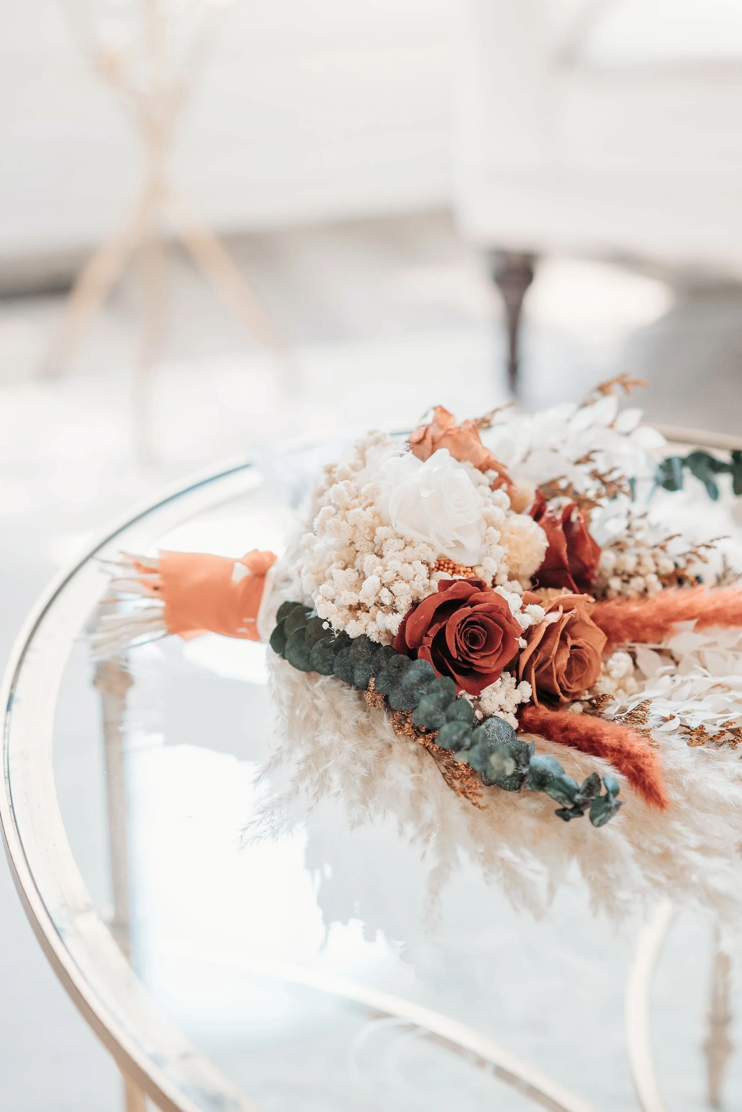 A floral arrangement with roses, dried leaves, and fluffy blooms on a reflective glass table.