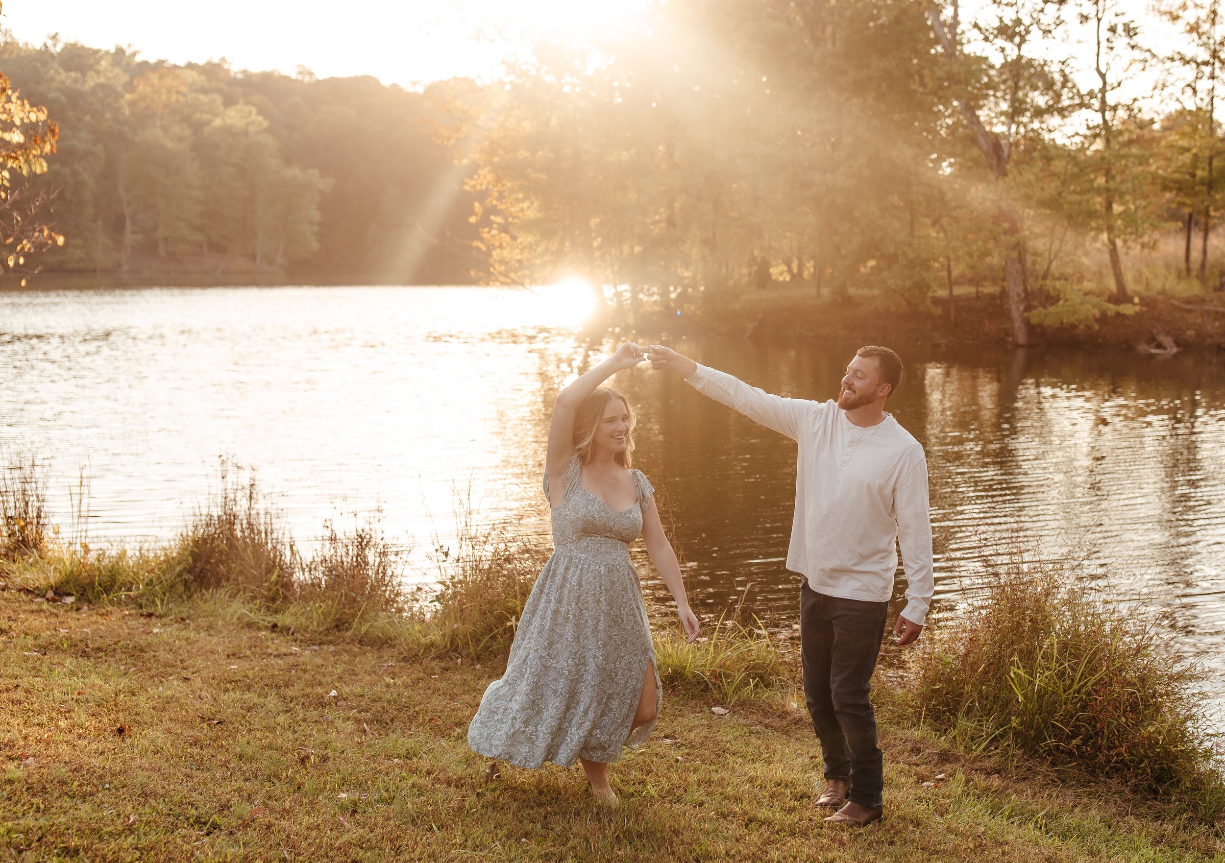 A couple dancing by a lake during sunset, with the man twirling the woman.