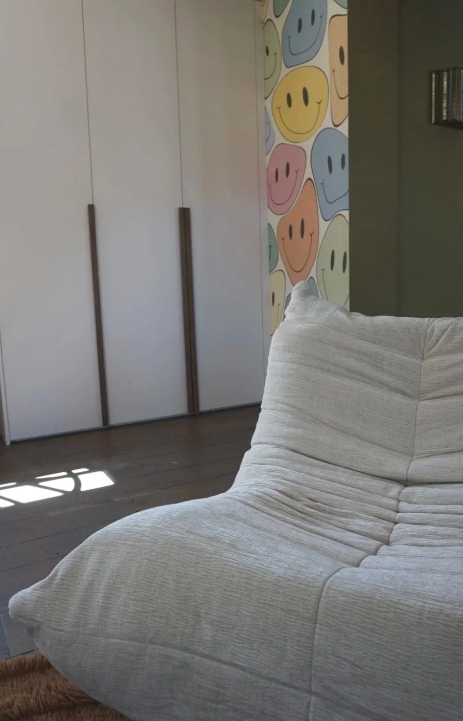 Een kamer met een witte kast, een muur met kleurrijke smiley gezichtjes en een beige bank.