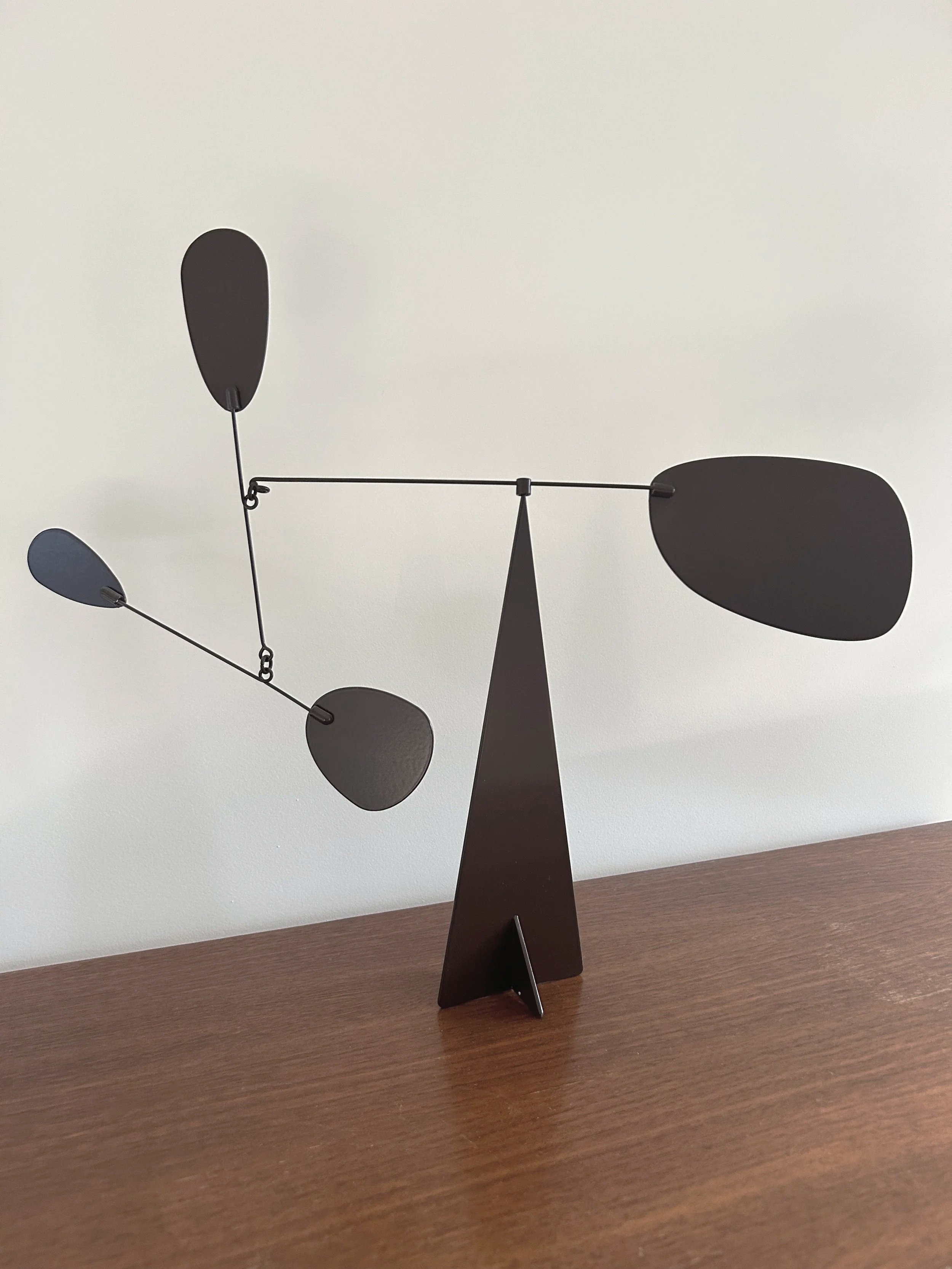 Een moderne black metal ontwerpweegschaal met metalen ballen en een driehoekige steun, geplaatst op een houten oppervlak.