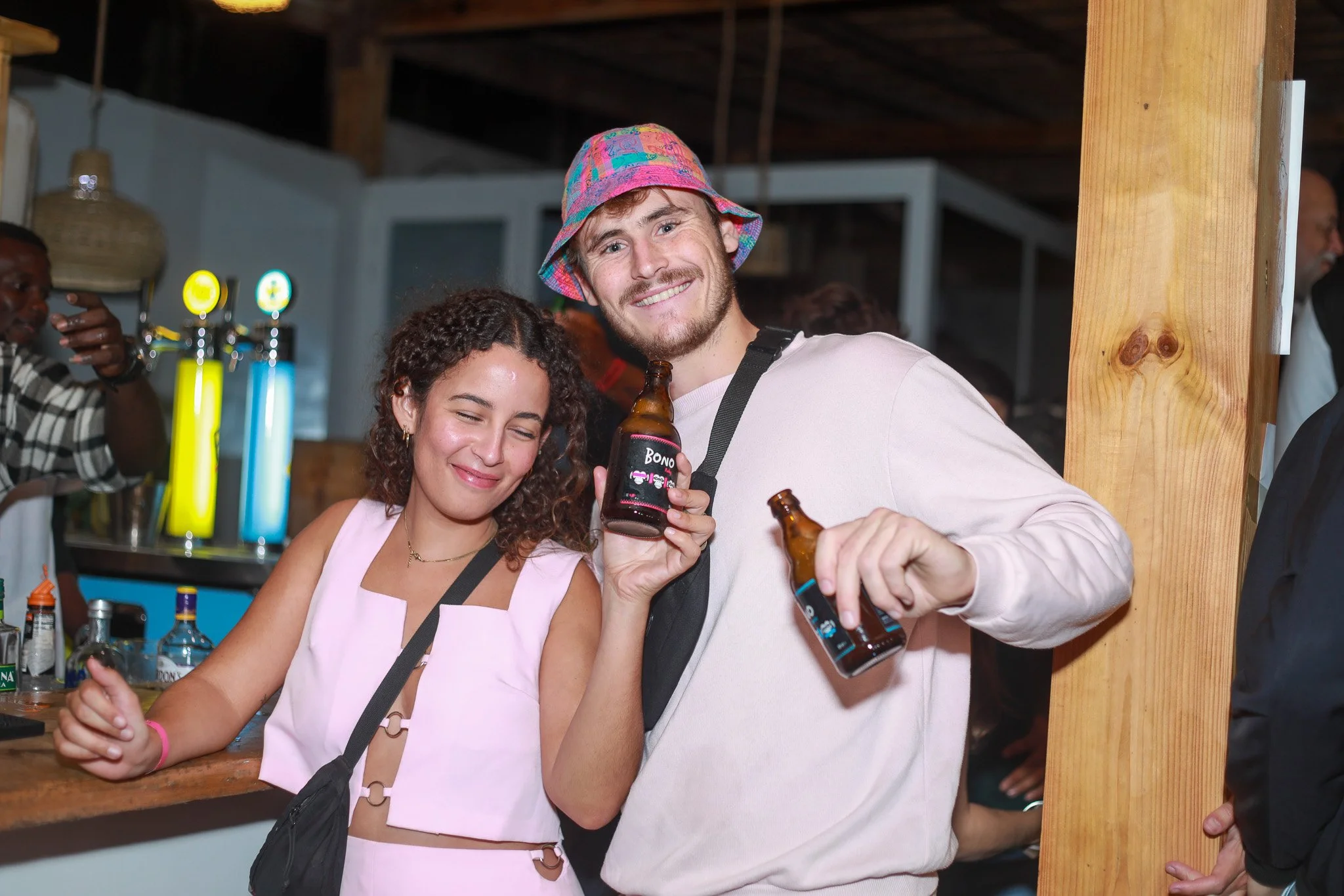 Two happy people wearing pink at a bar holding beer bottles