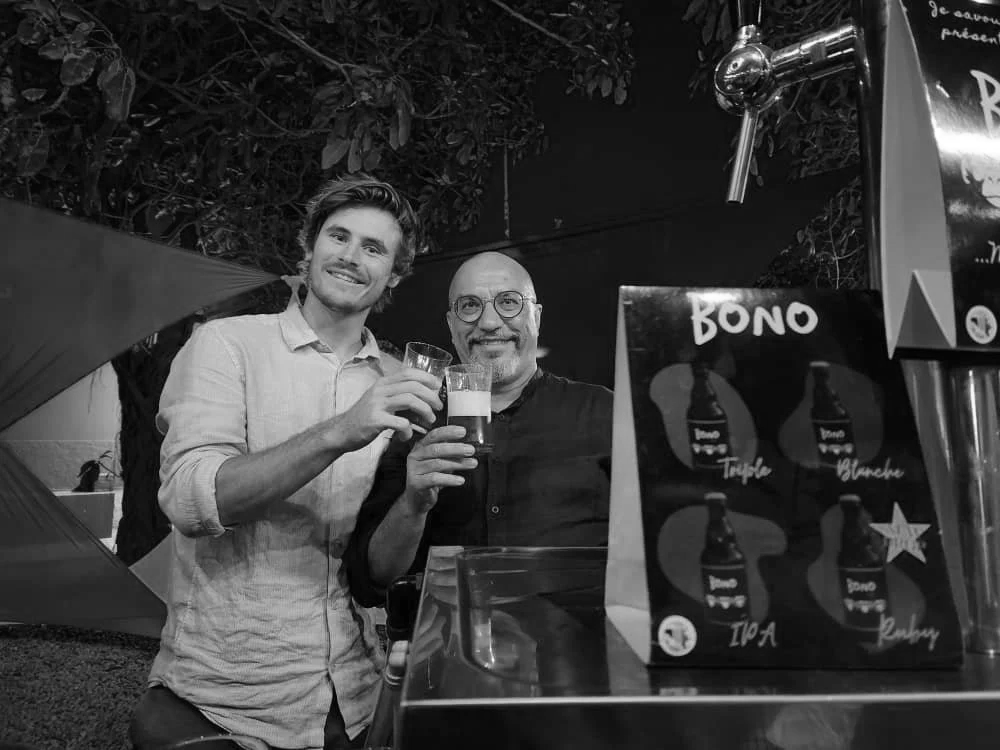 Two men holding beer glasses and cheering while smiling at the camera