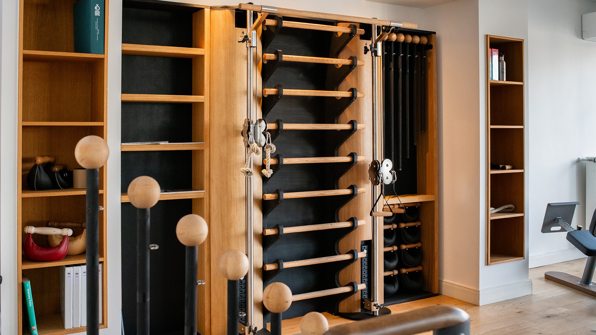 Krafttraining- und Fitnessgeräte in einem Heimtrainingsraum, inklusive Kettlebells, Hanteln, Sprossenwand und mit Wasser gefüllte Flaschen auf einer Wandhalterung.