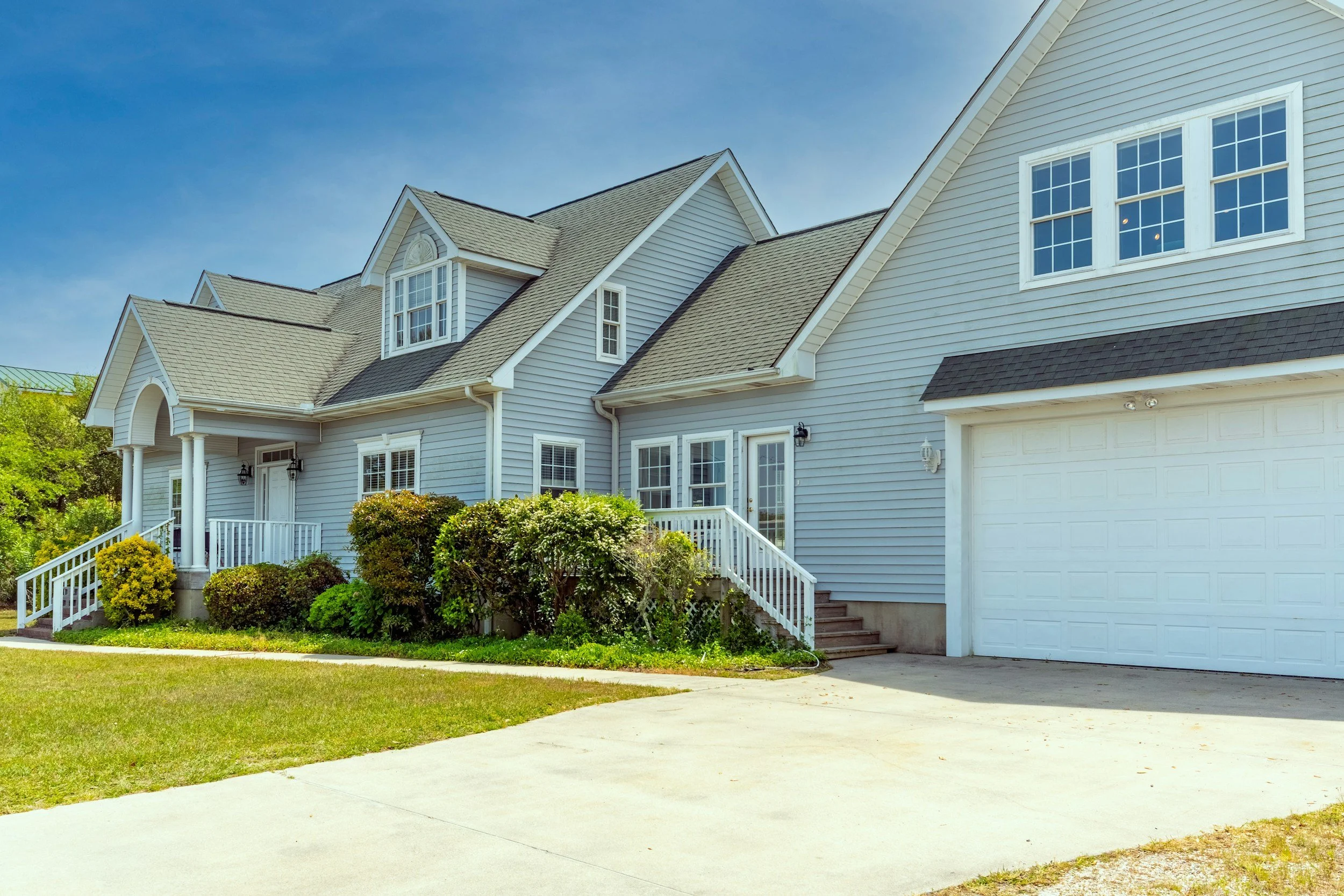 A large, light-blue, two-story suburban house with a well-maintained front yard and driveway