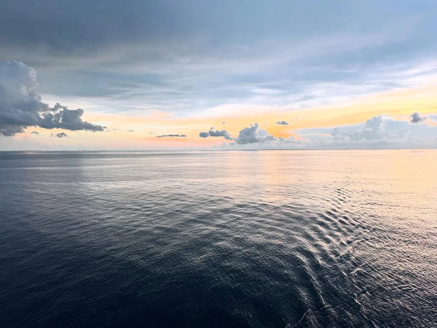 Calm ocean waters under a partly cloudy sky at sunset or sunrise, with soft pastel colors.