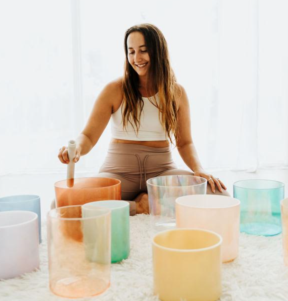 A woman playing colorful singing bowls with a mallet in a bright room.