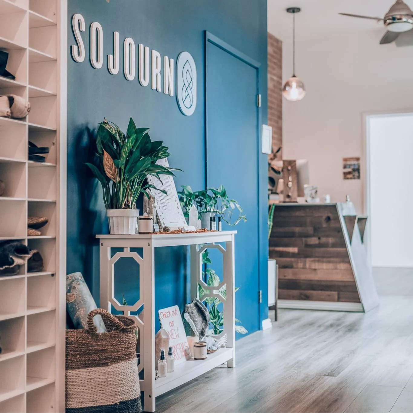 Decorative interior with a blue wall, white shelf, indoor plants, and sign that says 'Sojourn'