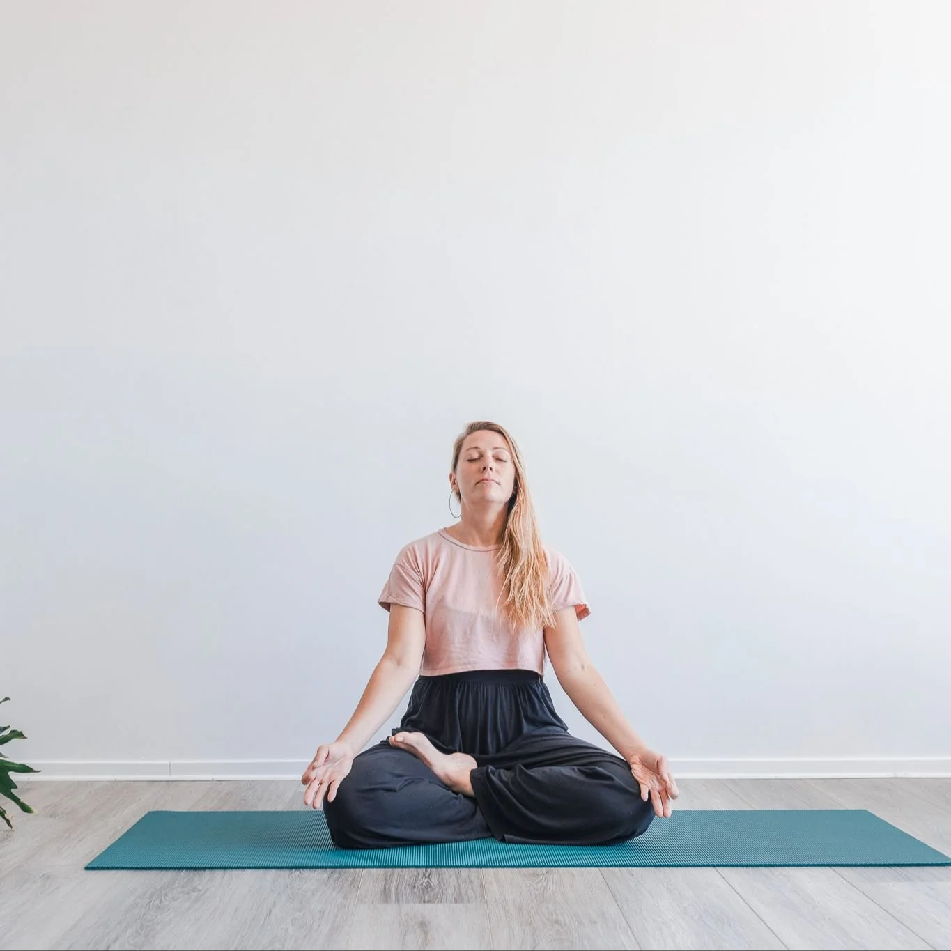 A woman practicing yoga in a seated meditative pose on a blue yoga mat in a bright, minimalistic room.