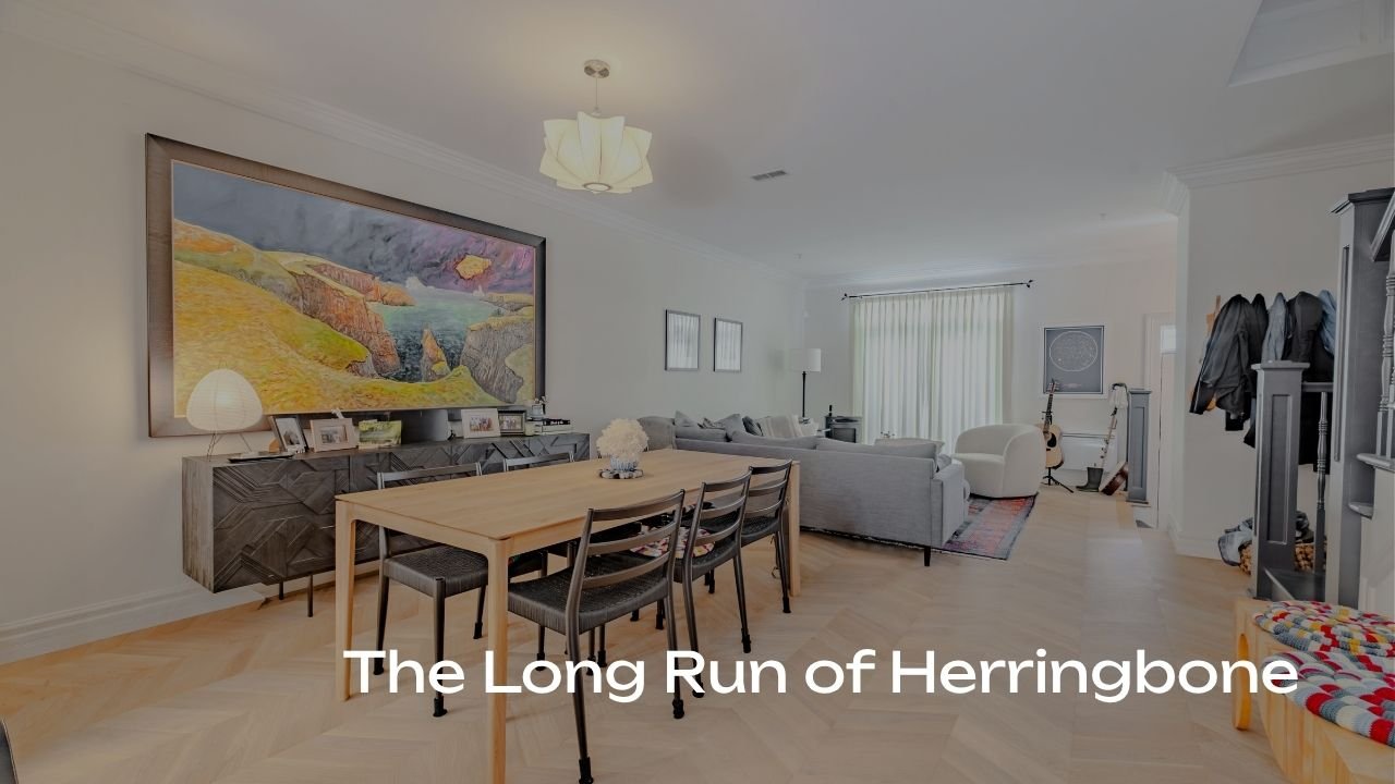 A spacious living room and dining area with light-colored walls and hardwood floors, featuring a large painting, a dining table with chairs, a sofa, armchair, guitar, and decorative items.