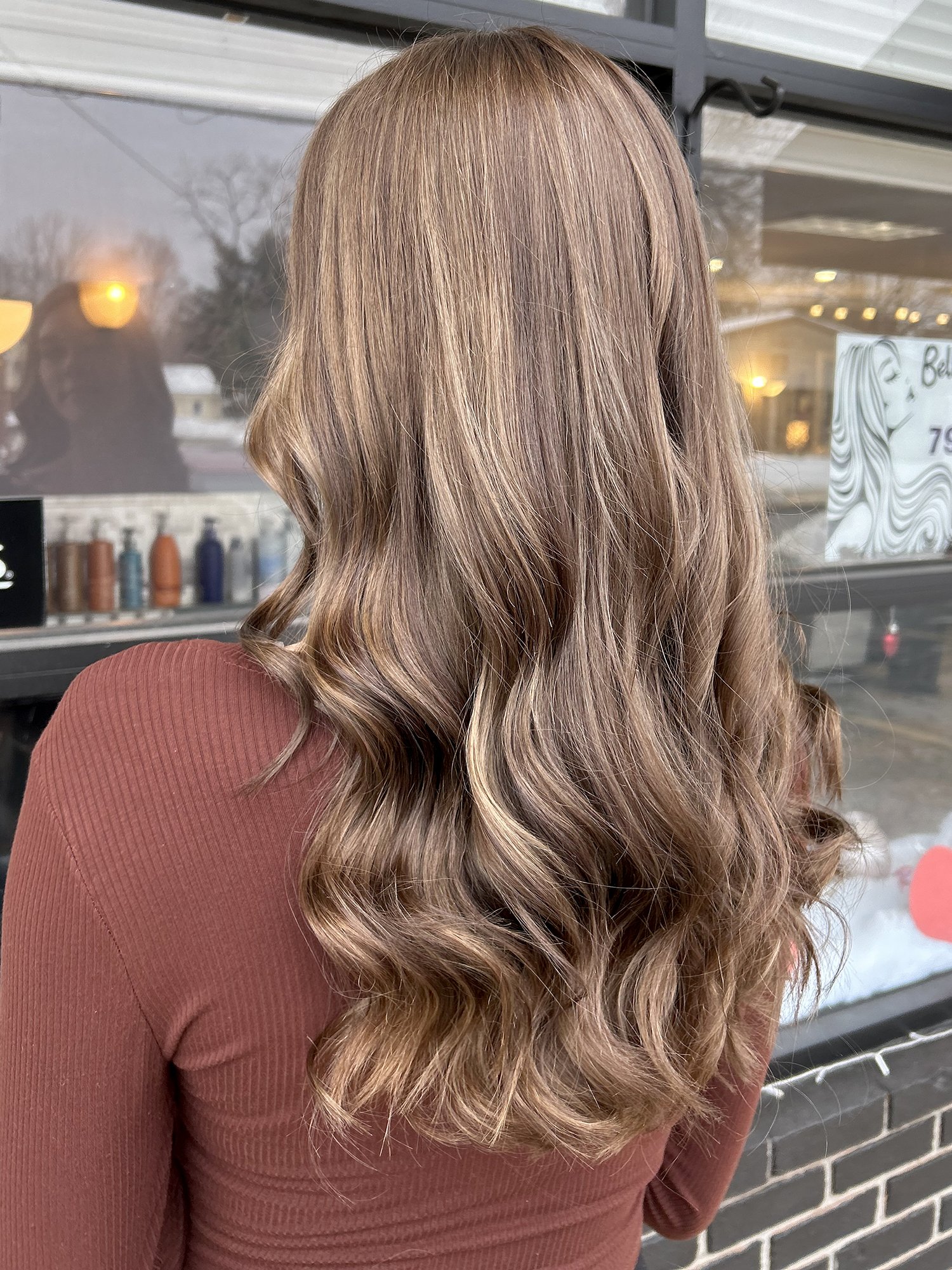 Long mid-brown hairstyle with highlights and waves.