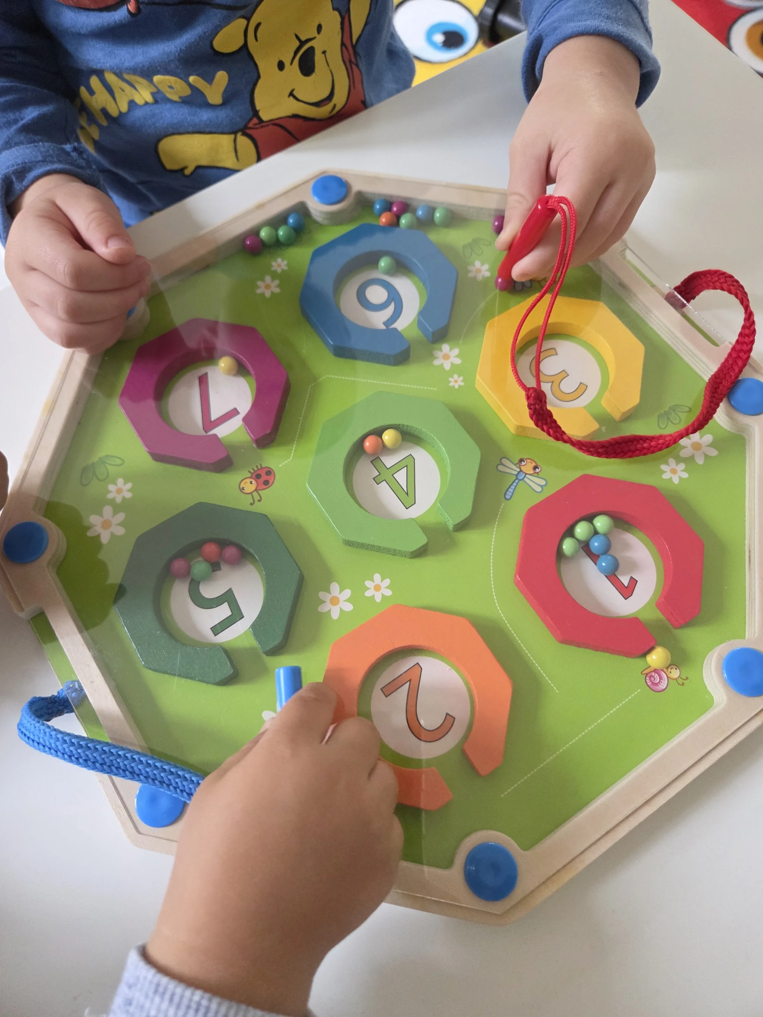 Two children playing a colorful maze game with numbered and lettered sections and small beads.