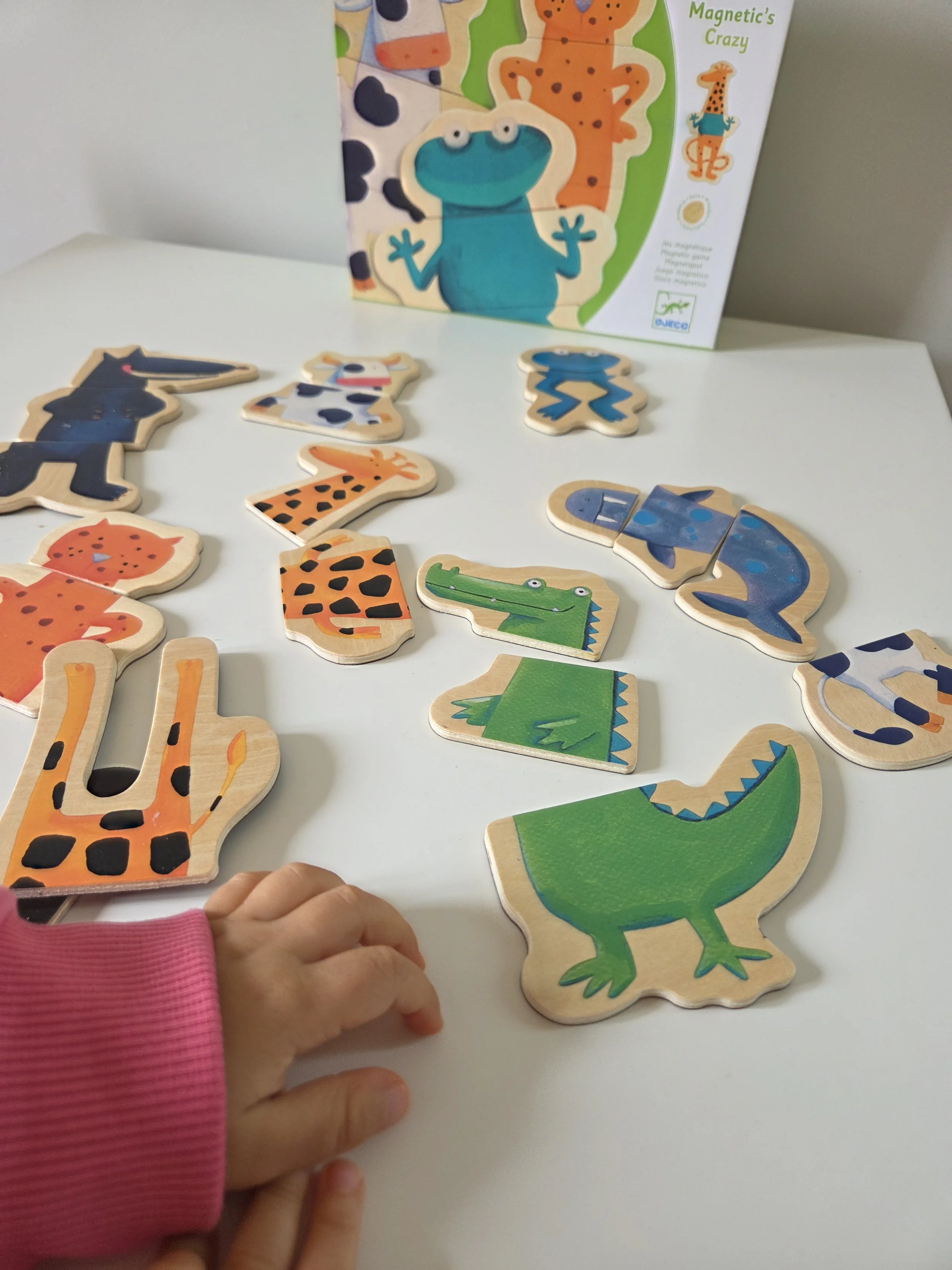 Children's puzzle featuring colorful jungle animals such as a crocodile, giraffe, crocodile, zebra, and hippo, on a white surface with a box in the background.