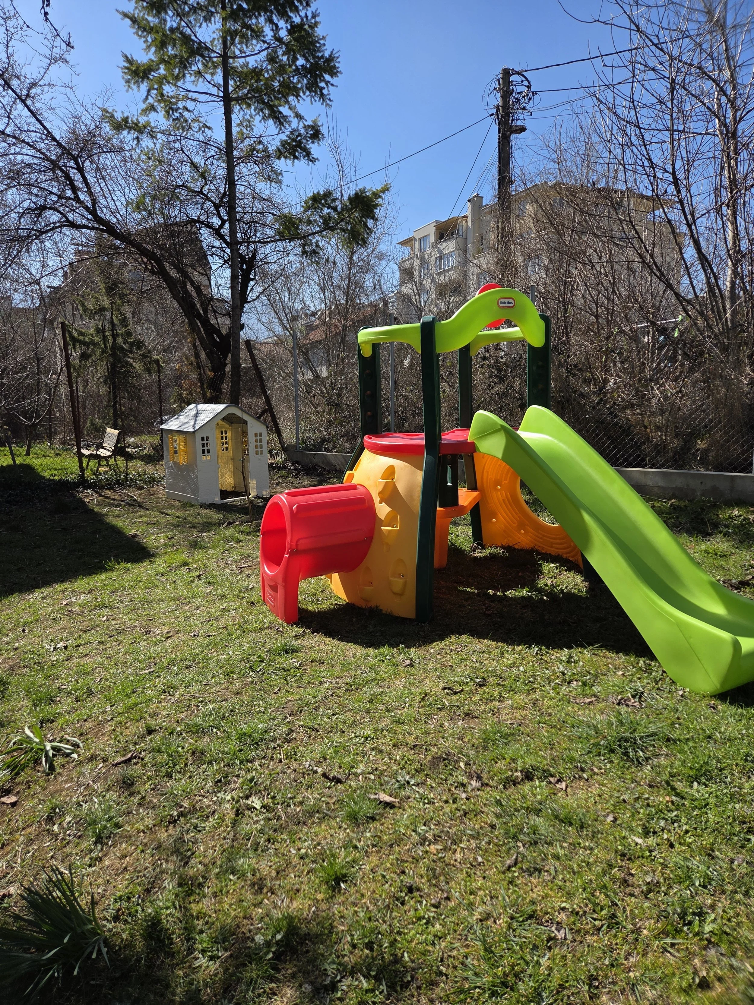 Colorful plastic playhouse with a slide and tunnel in a backyard on a sunny day