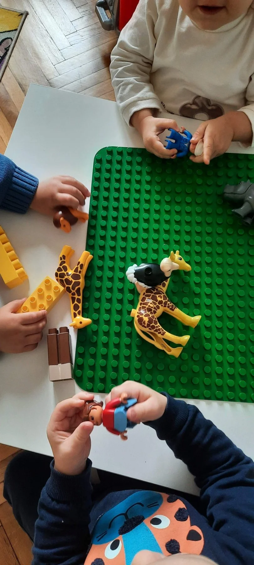 Children playing with toy animal figures on a LEGO baseplate.
