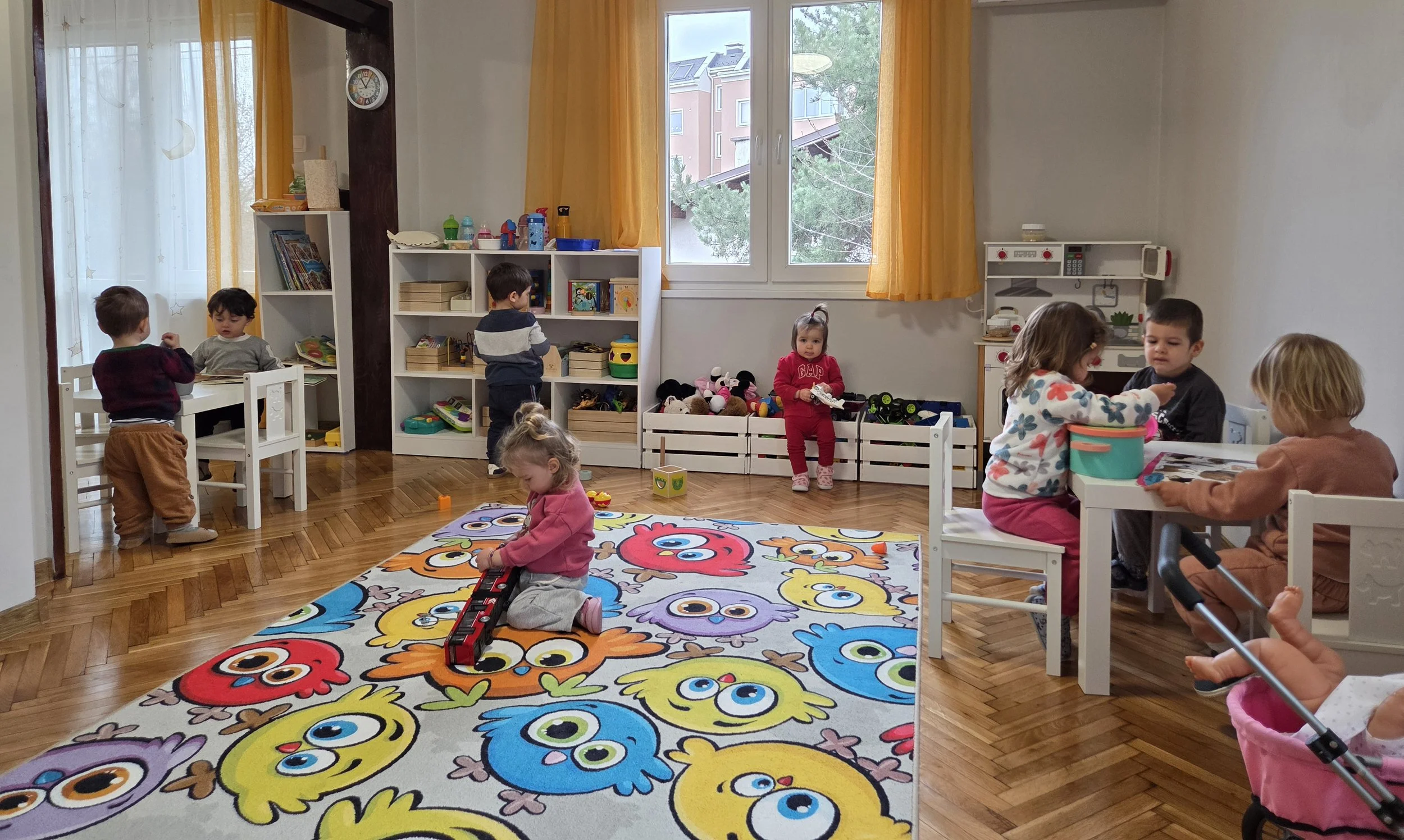 Children playing and engaging in activities in a brightly lit daycare or preschool classroom with colorful decor and toys.