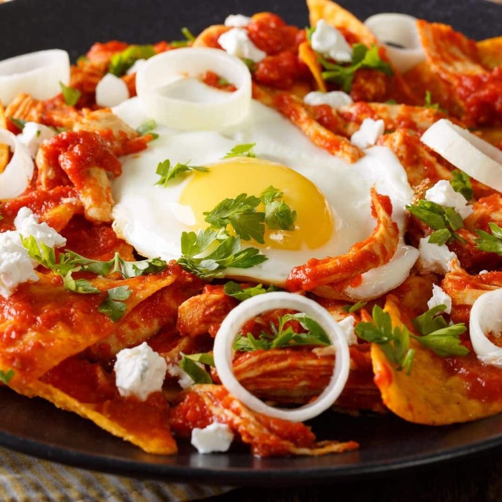 Close-up of a plate of nachos topped with melted cheese, sliced onions, fresh cilantro, sour cream, and a fried egg